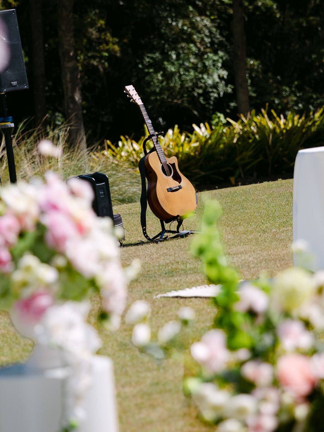 Acoustic guitar resting on stand at outdoor wedding ceremony surrounded by lush greenery and floral arrangements.