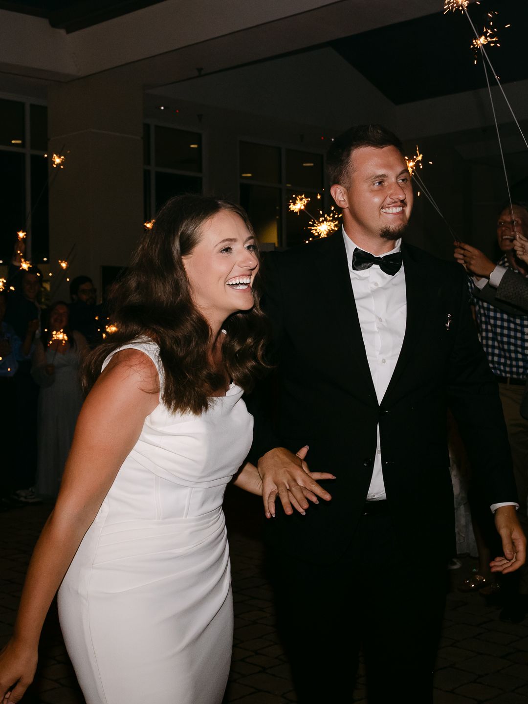 Bride and groom smiling during sparkler wedding reception exit, bride in white dress, groom in black tuxedo.