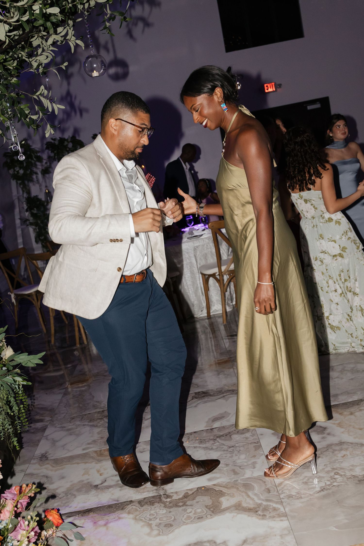 Man in beige blazer dances with woman in gold dress at elegant wedding reception.