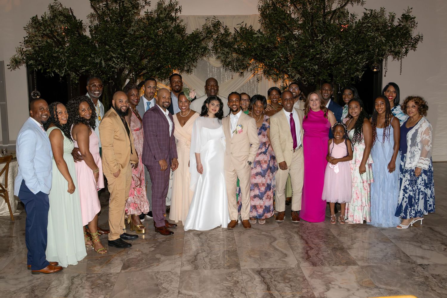 Large family group photo with bride and groom at outdoor evening wedding reception.