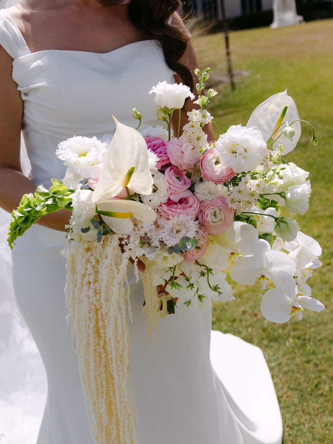 Elegant bridal bouquet featuring white calla lilies, pink ranunculus, orchids, and cascading pearl strands held outdoors.
