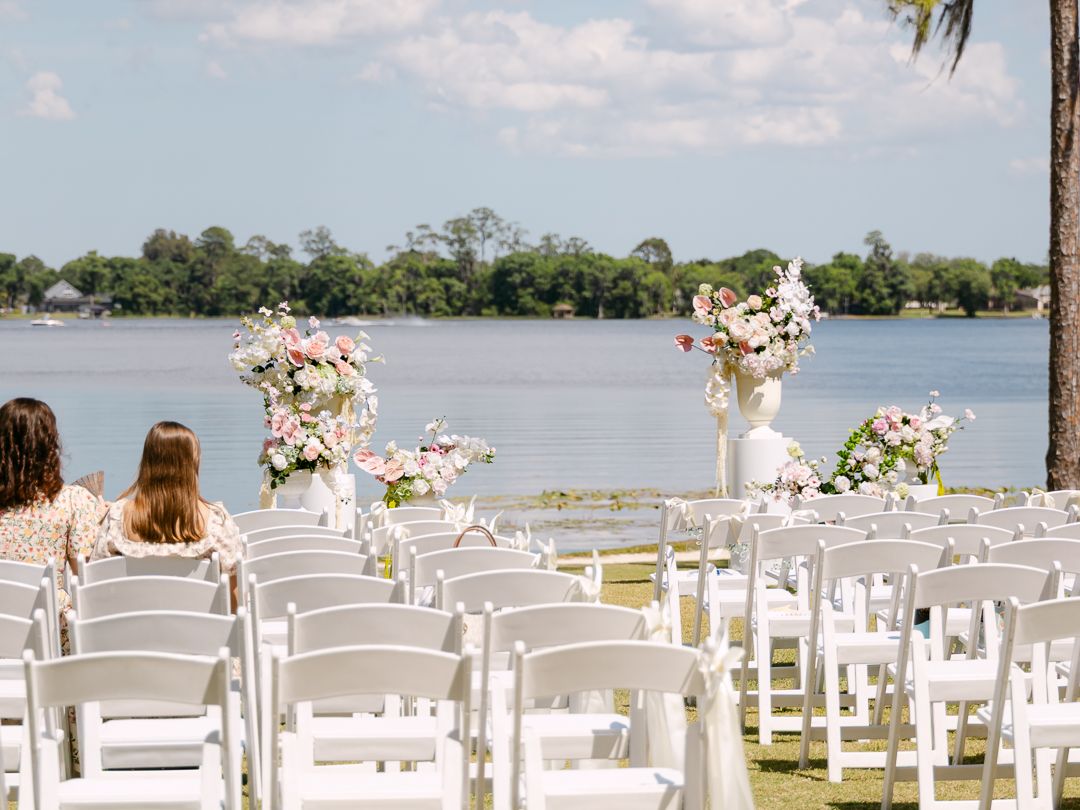 Elegant outdoor wedding ceremony setup with white chairs and floral arrangements overlooking a serene lakeside view.