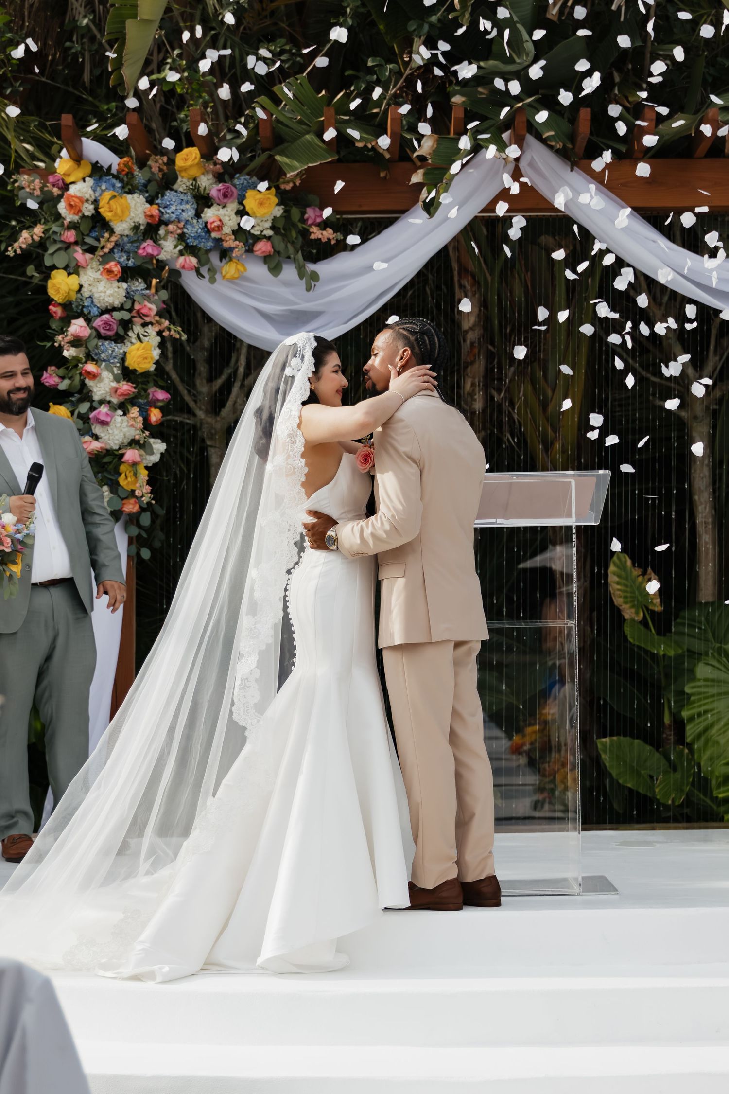 Bride and groom share first kiss at outdoor wedding altar adorned with colorful floral arrangements.