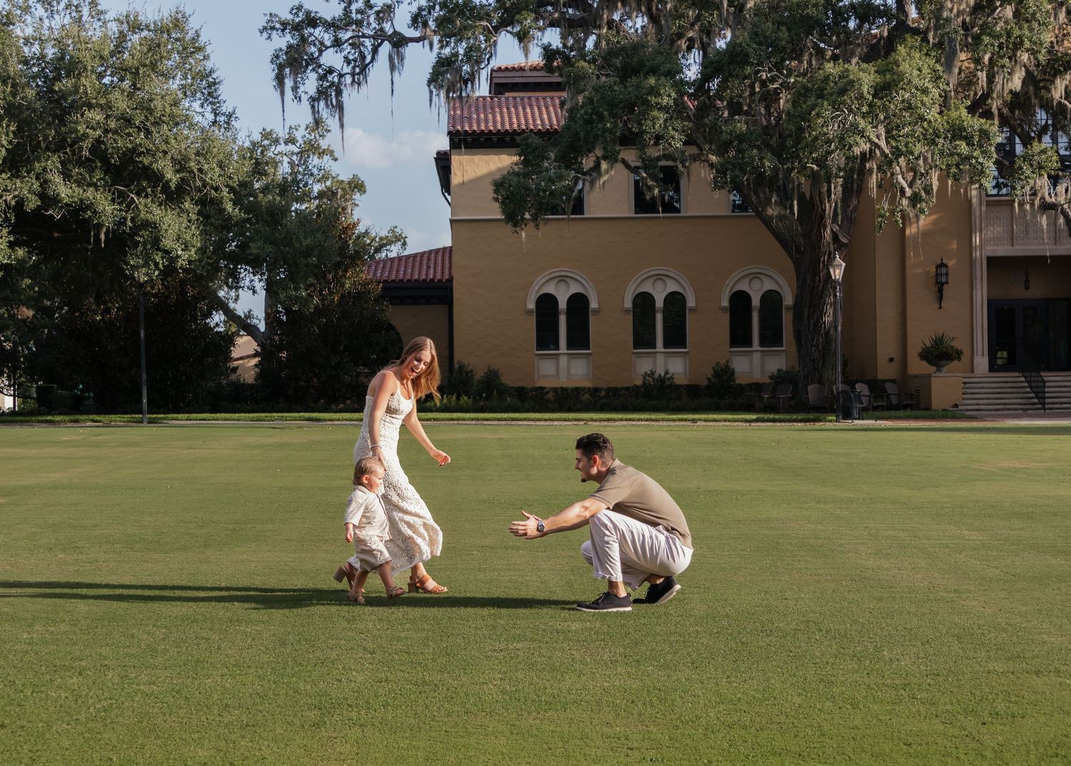 Couple sharing a joyful moment on lush green lawn outside an elegant estate building surrounded by trees.