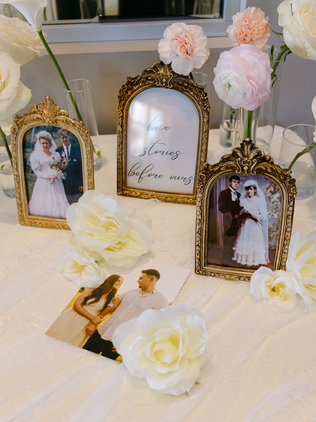 Gold ornate frames displaying vintage wedding photos arranged with white and pink flowers on a lace tablecloth at a wedding reception.