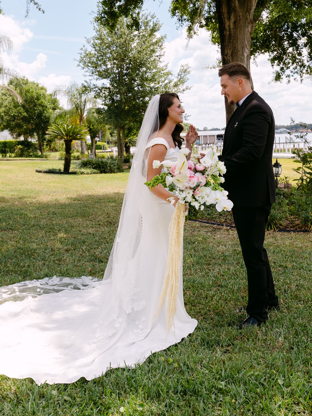 Bride and groom share first look outdoors, bride in white gown holding pink bouquet.