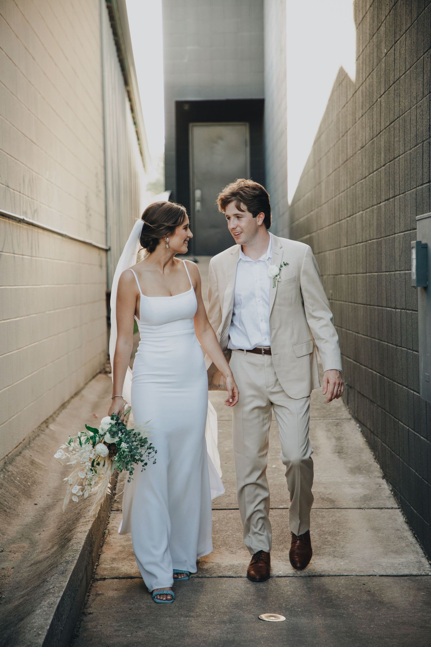 A couple in wedding attire walks together down a narrow alley between concrete walls in a series of artistic shots.