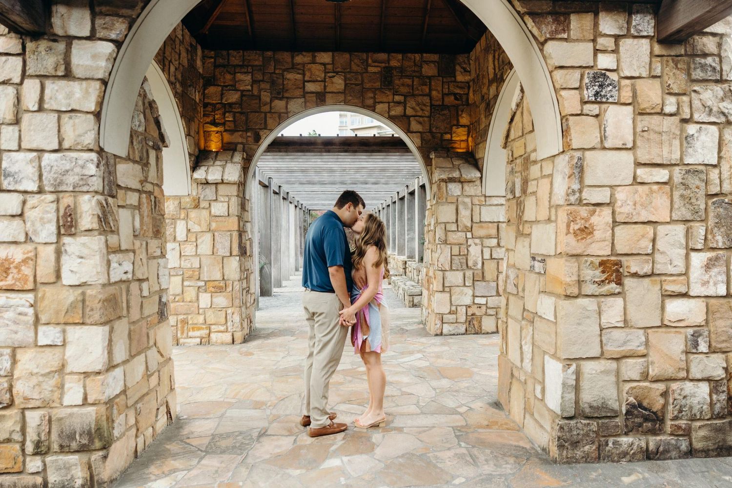 Couple sharing a romantic moment under stone archways at an outdoor venue, perfect for engagement or wedding photography.
