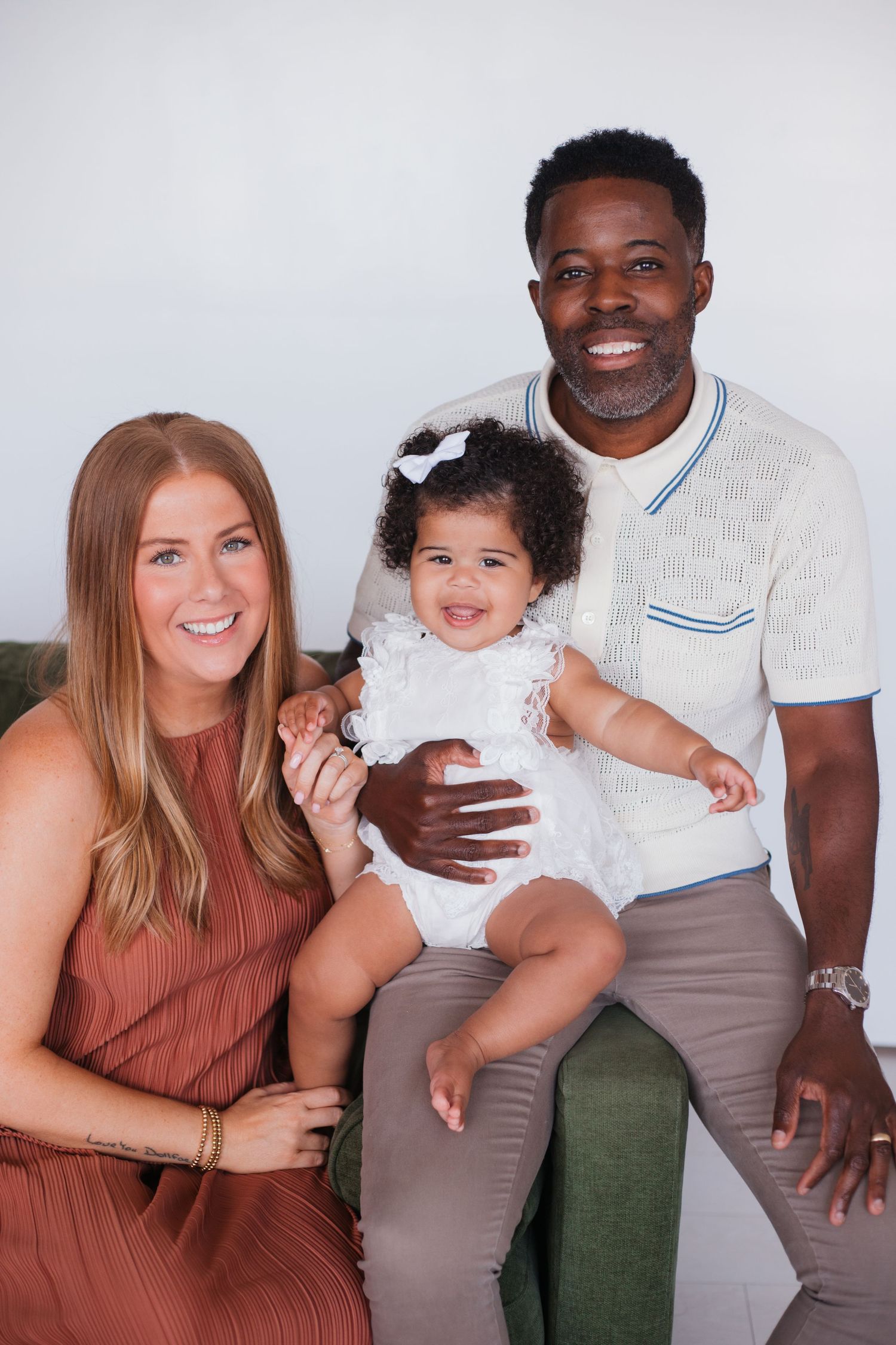 Family poses together on green couch for professional studio portrait.