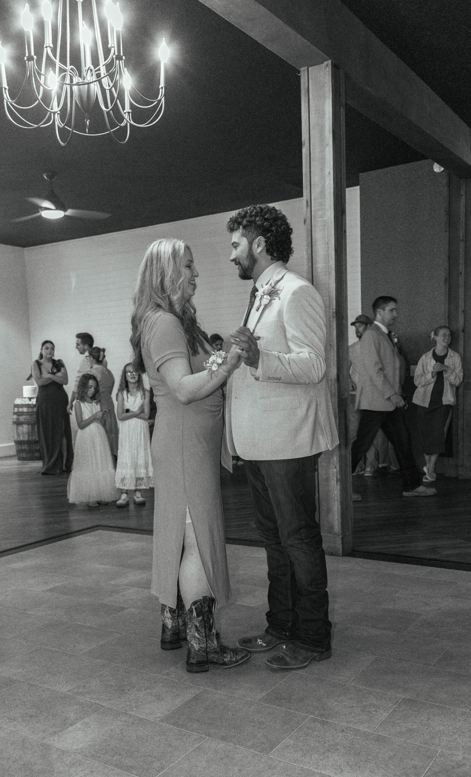Couple sharing first dance at wedding reception in rustic venue with chandelier, black and white photo.
