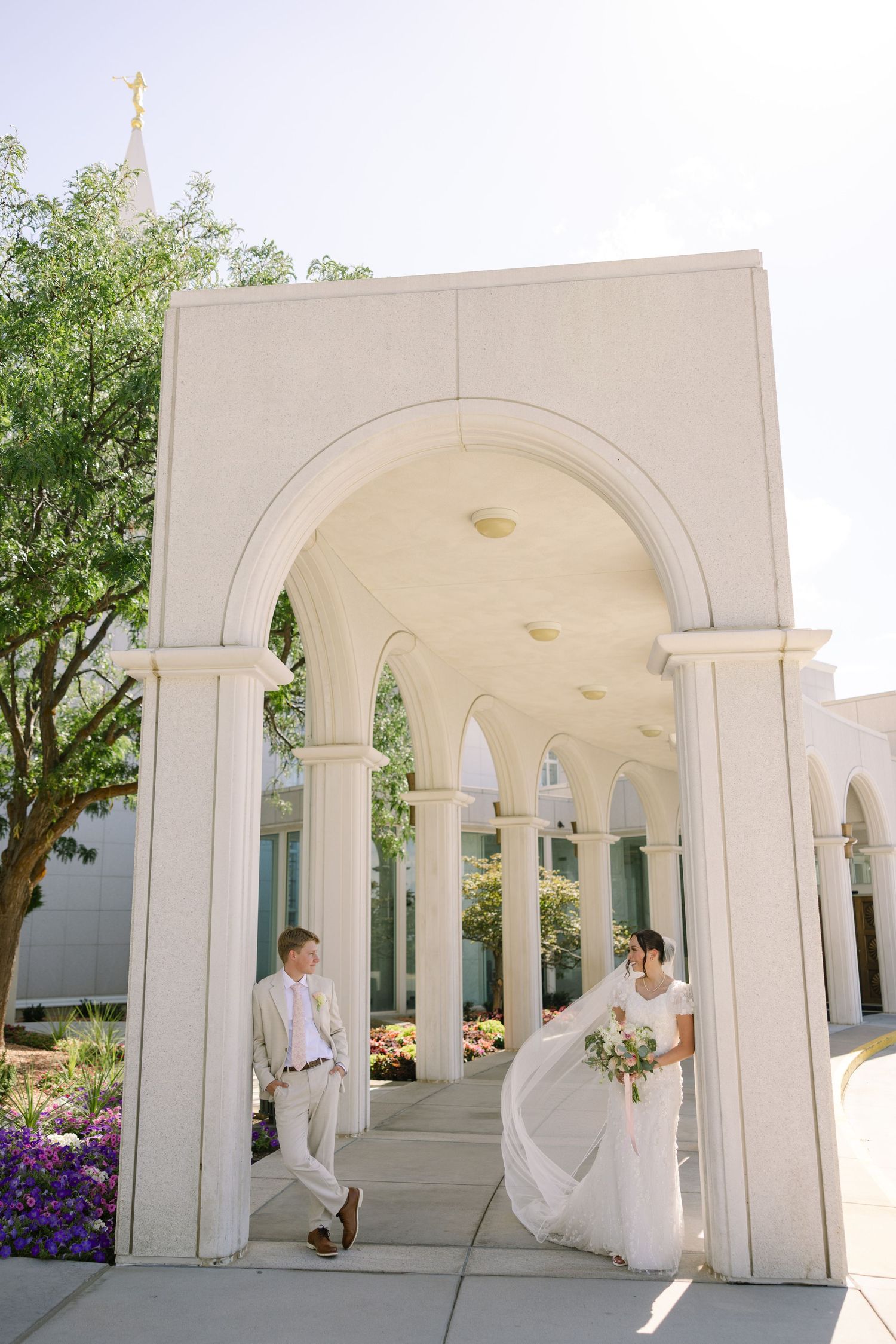 Bride and groom pose under elegant white arched colonnade outside an LDS temple on their wedding day.