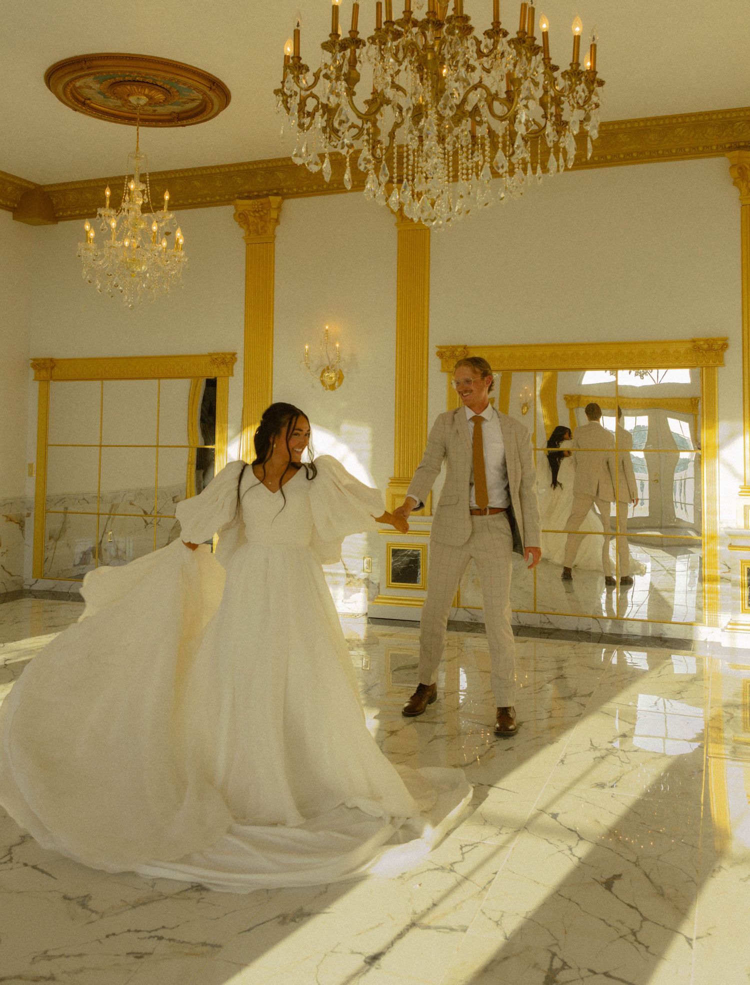 Bride and groom dancing in elegant gold and marble ballroom with crystal chandeliers during wedding reception.