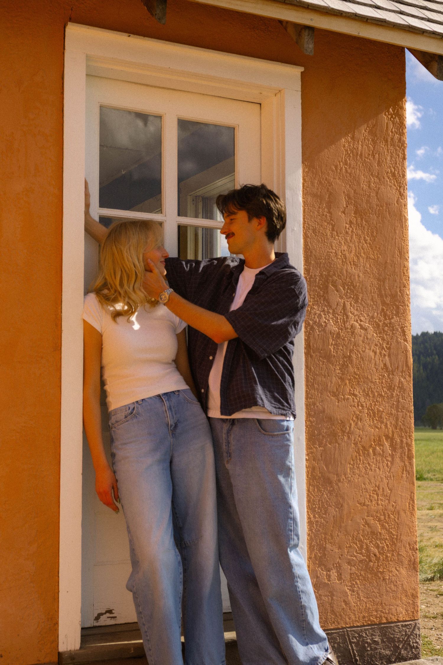 Young couple sharing a romantic moment by an orange building doorway on a sunny day.