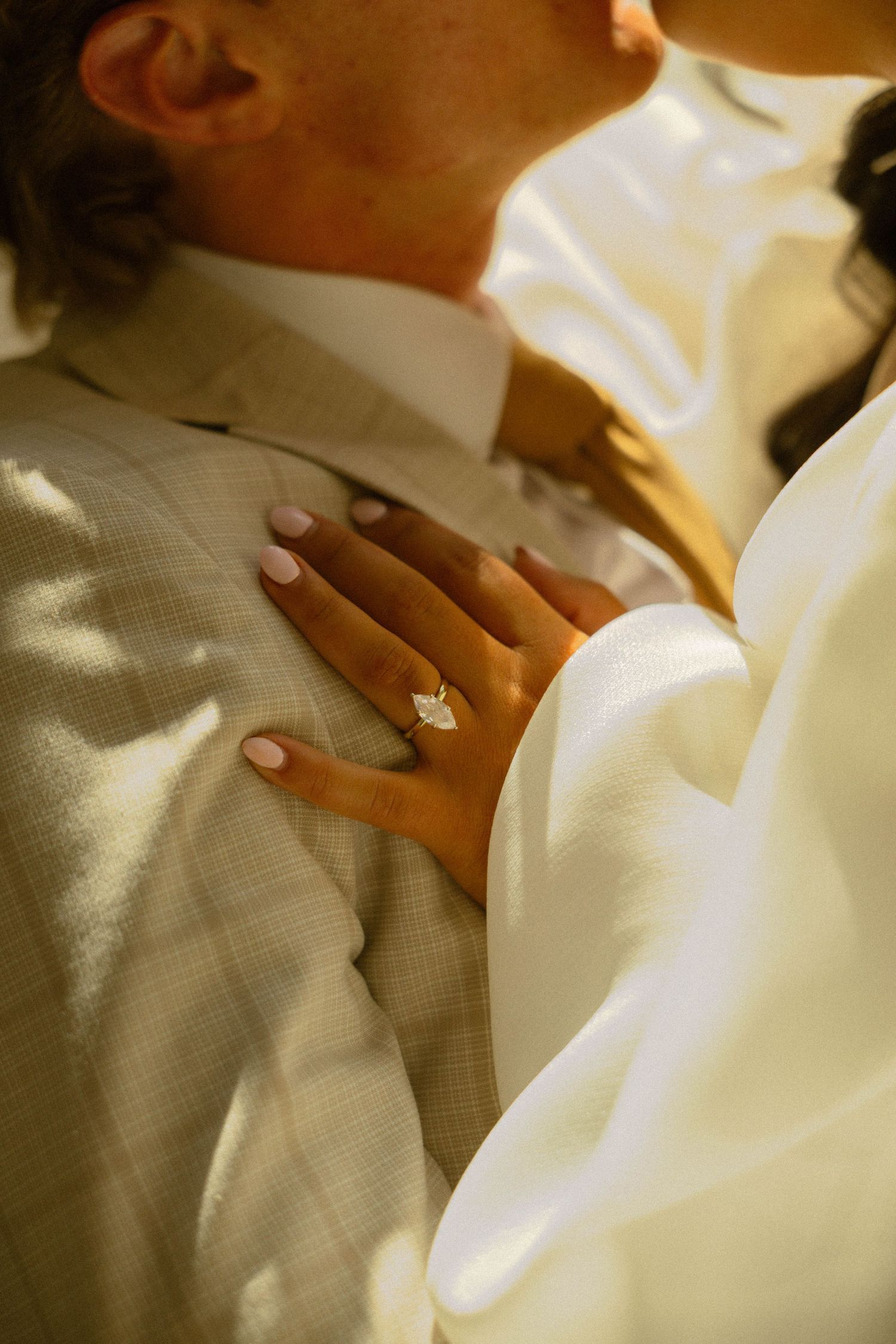 Bride's hand with diamond engagement ring resting on groom's suit during wedding ceremony kiss.