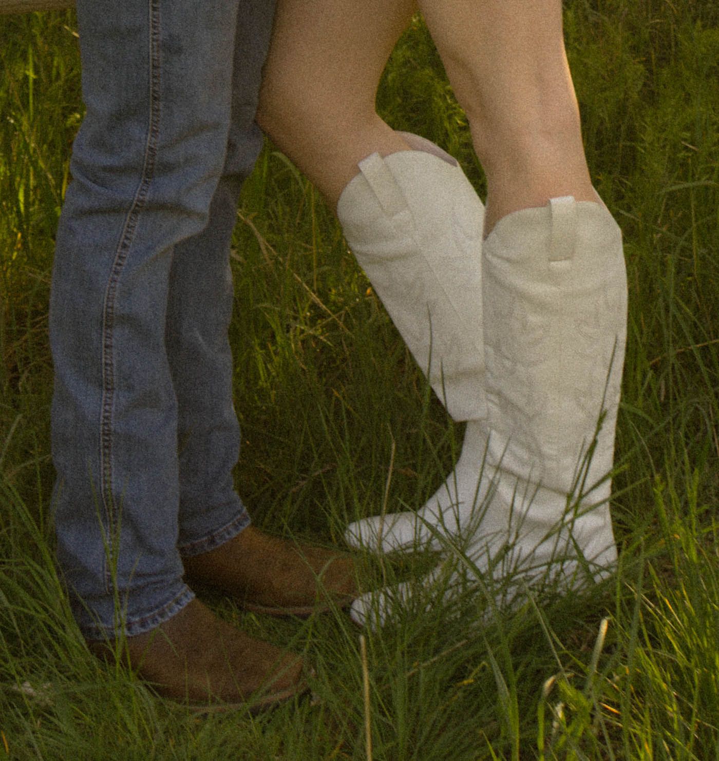 Two people standing in grass, one in jeans with brown cowboy boots and one in white cowboy boots.