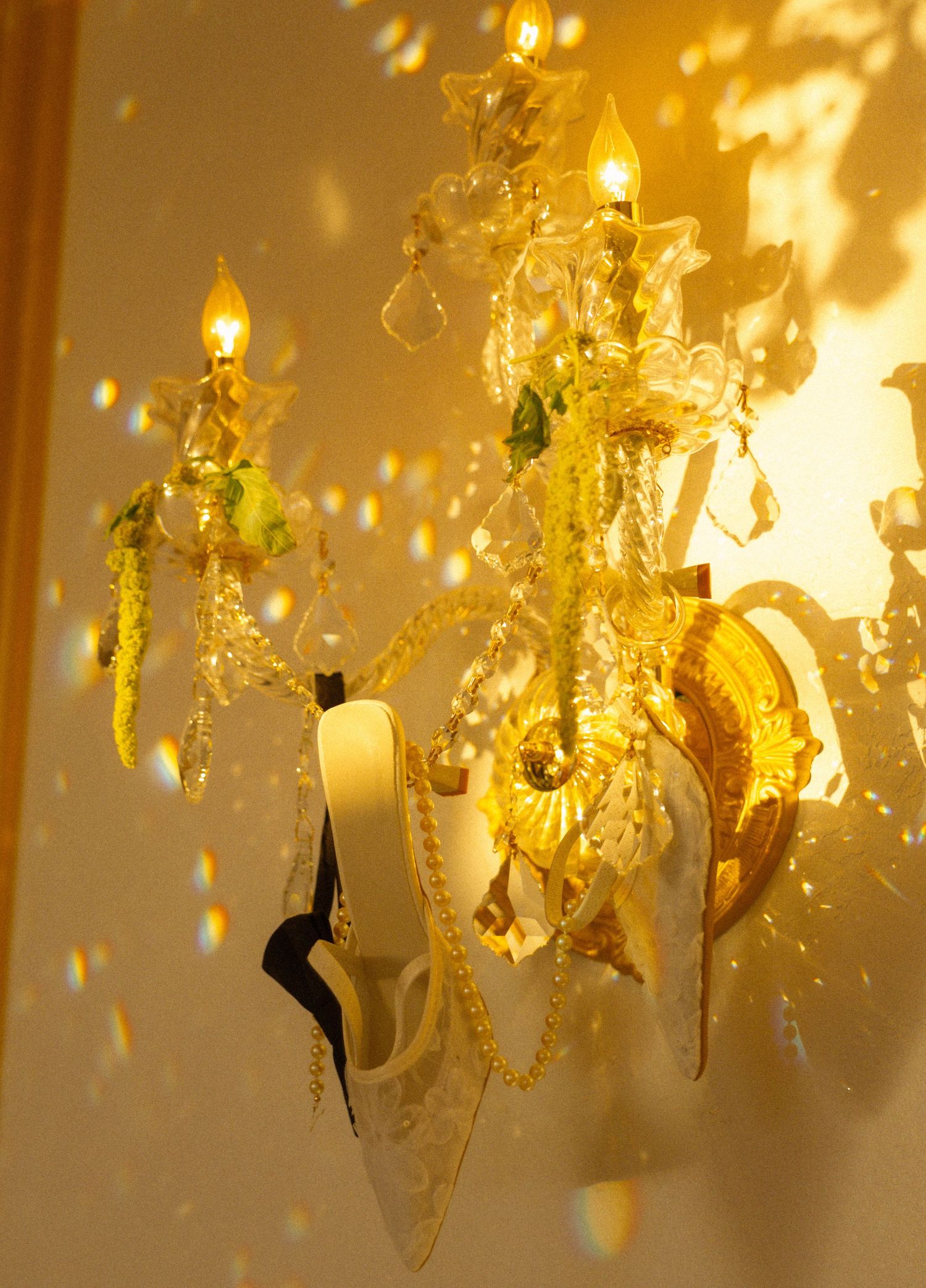 Elegant crystal wall sconce chandelier with glowing candle lights casting golden reflections on warm beige wall.