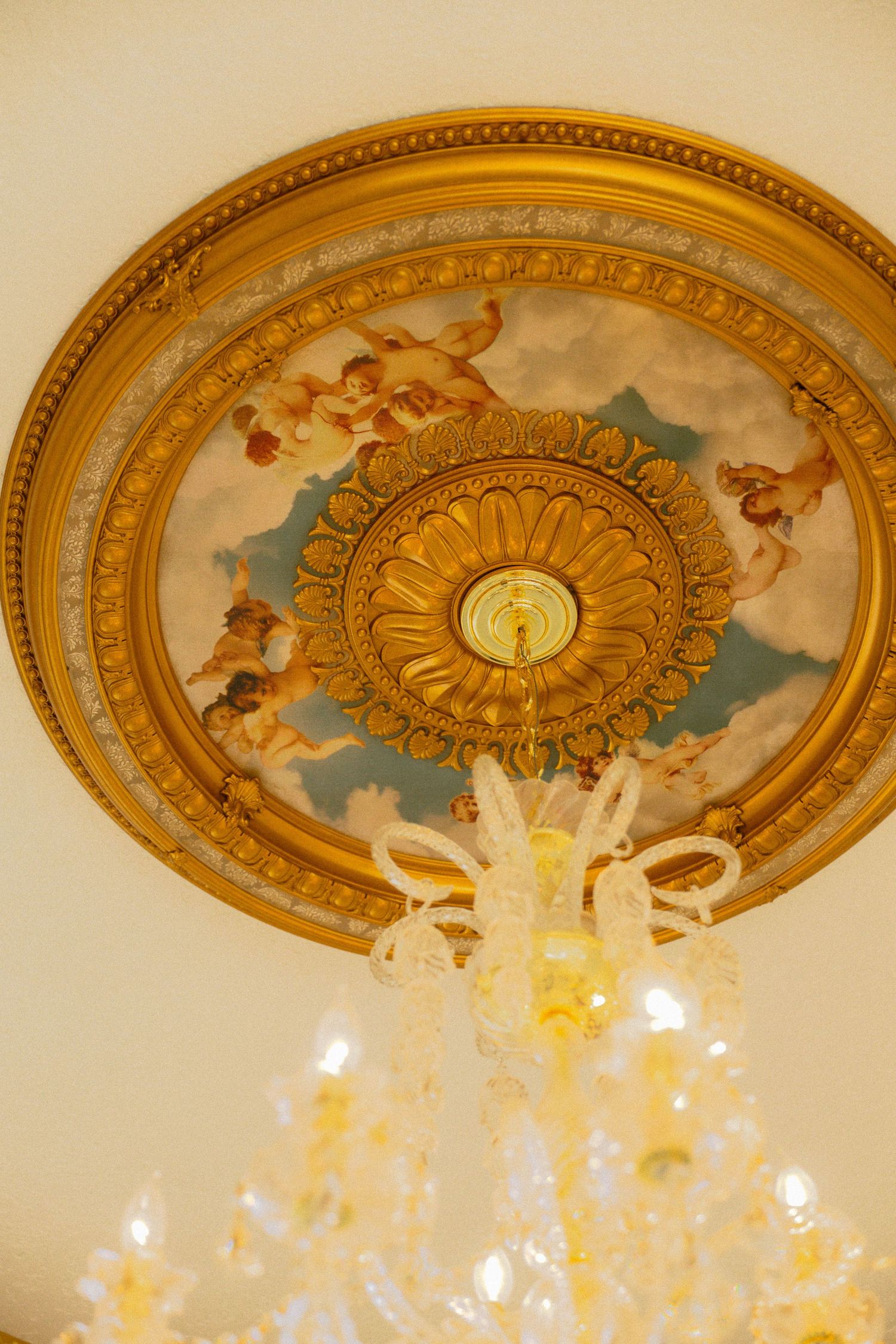 Ornate gold ceiling medallion with cherub fresco and elegant crystal chandelier in a classic interior.
