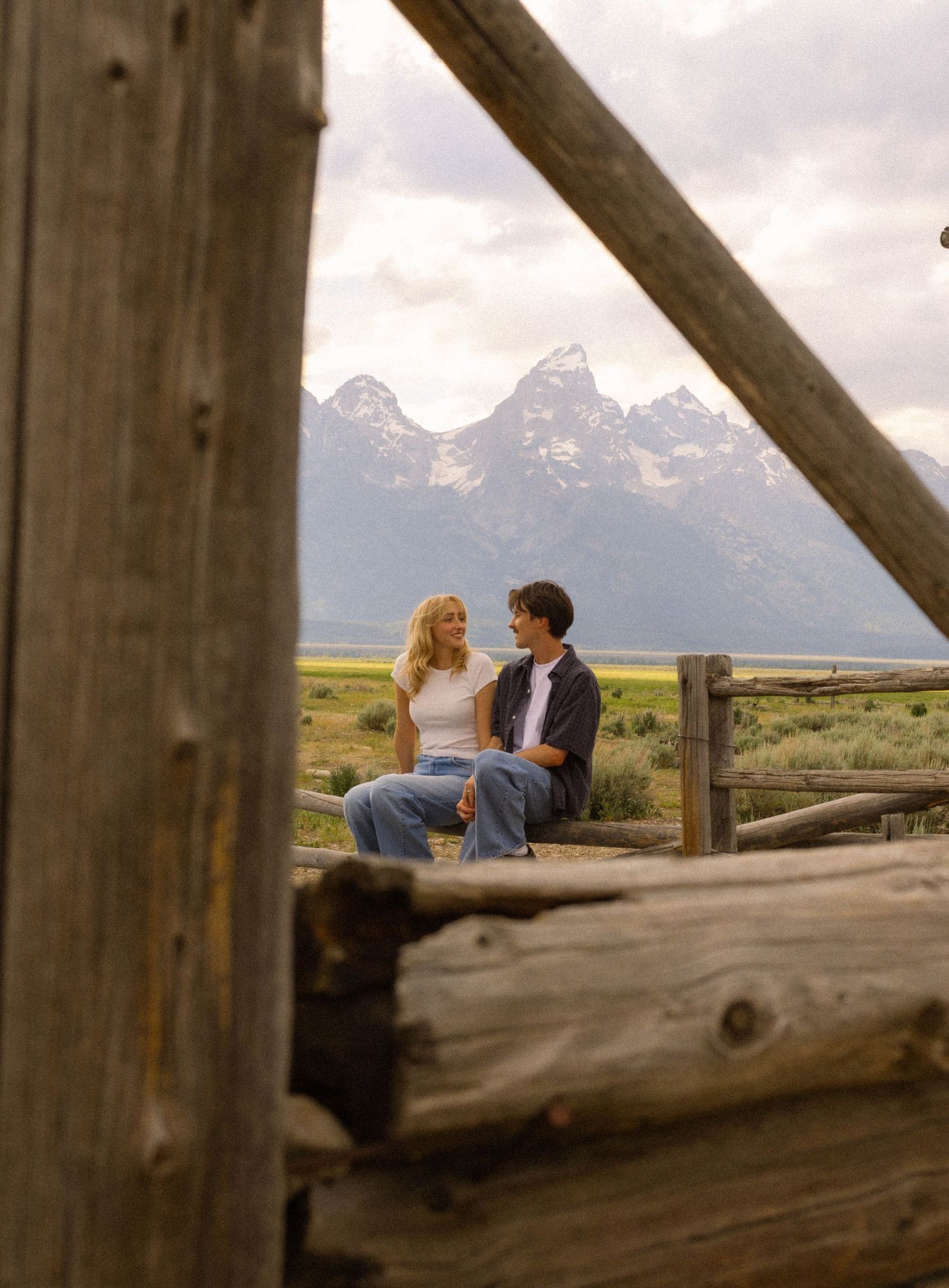 Couple sitting together on a wooden fence with majestic mountain range backdrop in Grand Teton National Park.
