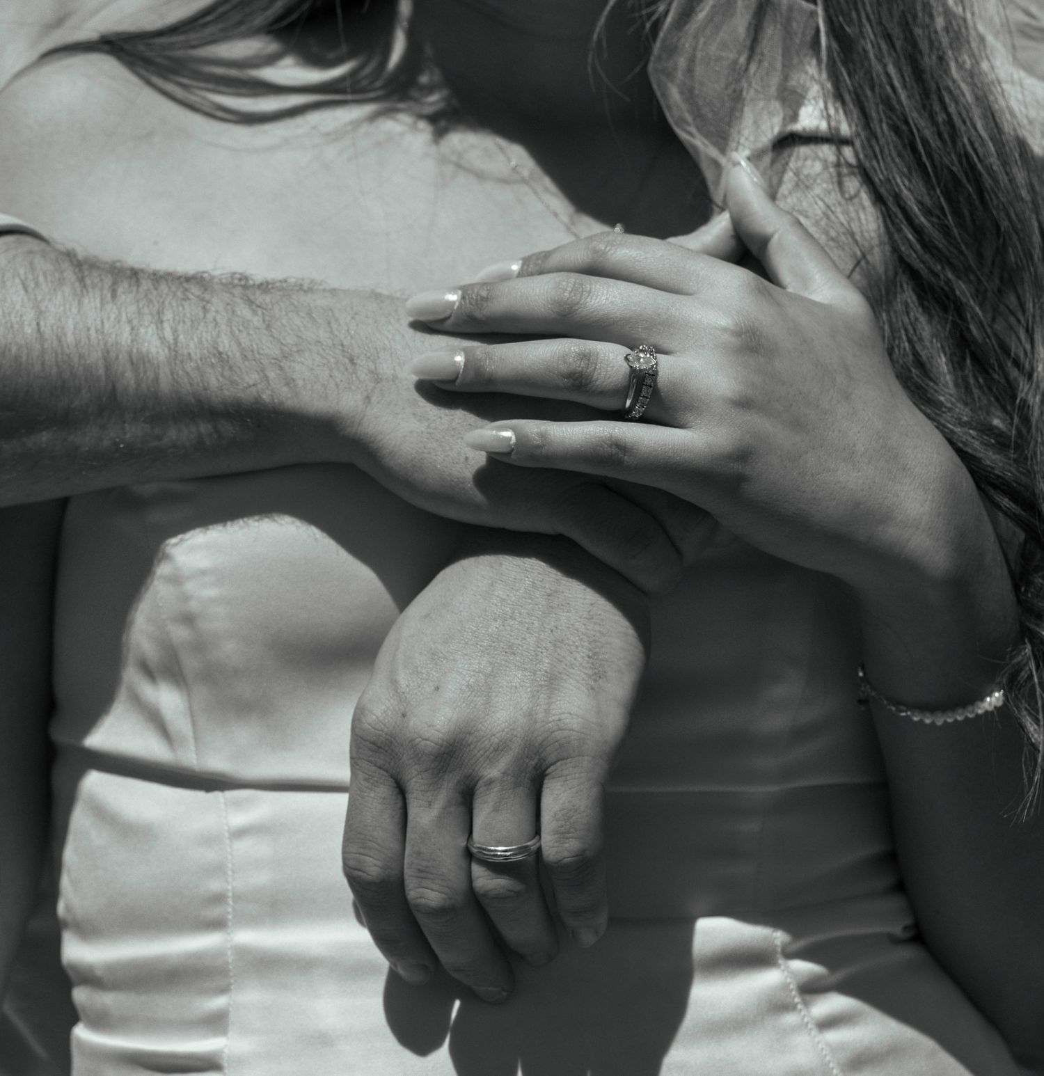 Black and white photo of a couple embracing, showcasing wedding rings on their hands, symbolizing love and marriage.