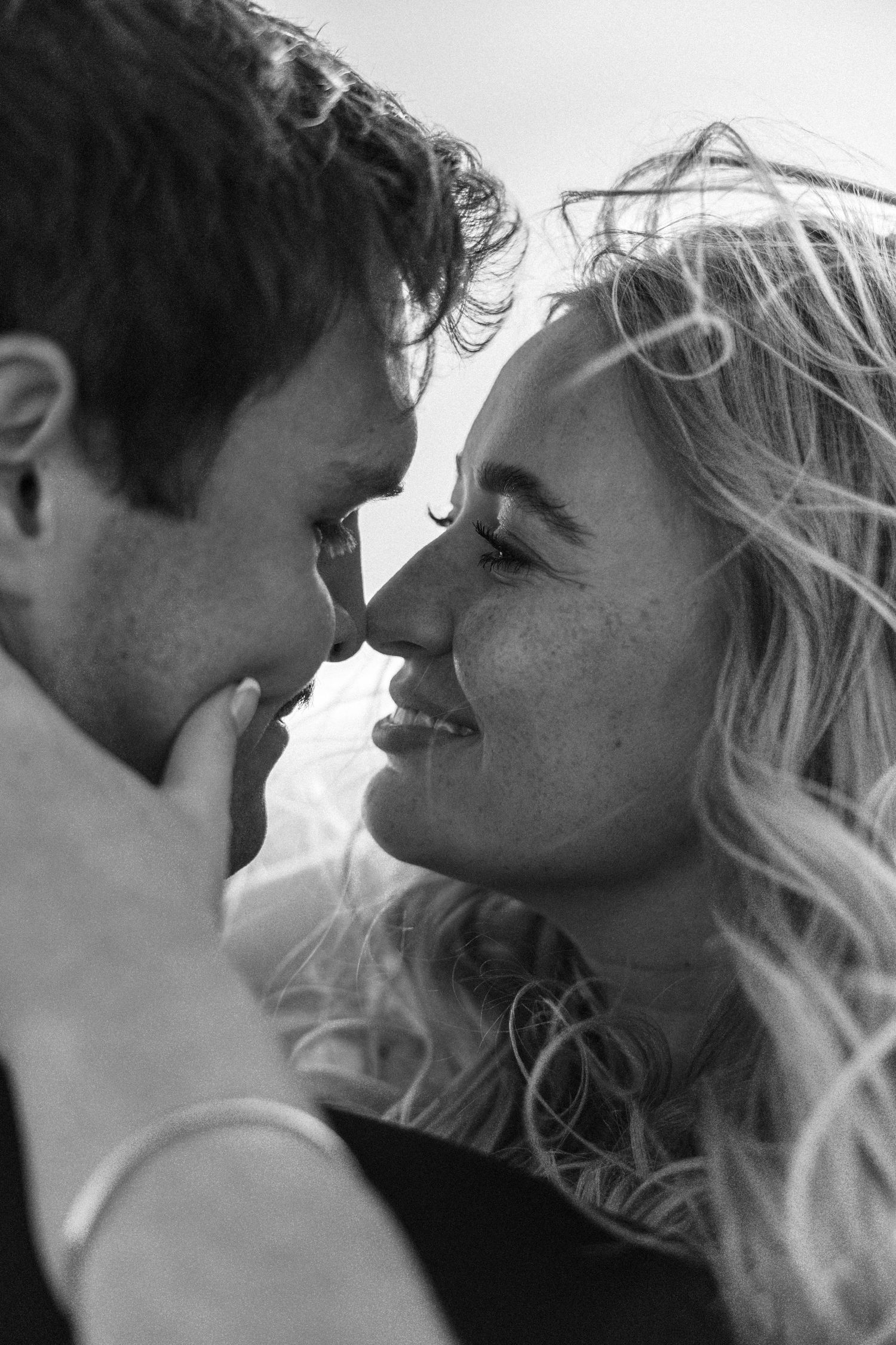 Black and white close-up of a smiling couple about to kiss, capturing a romantic and tender moment.