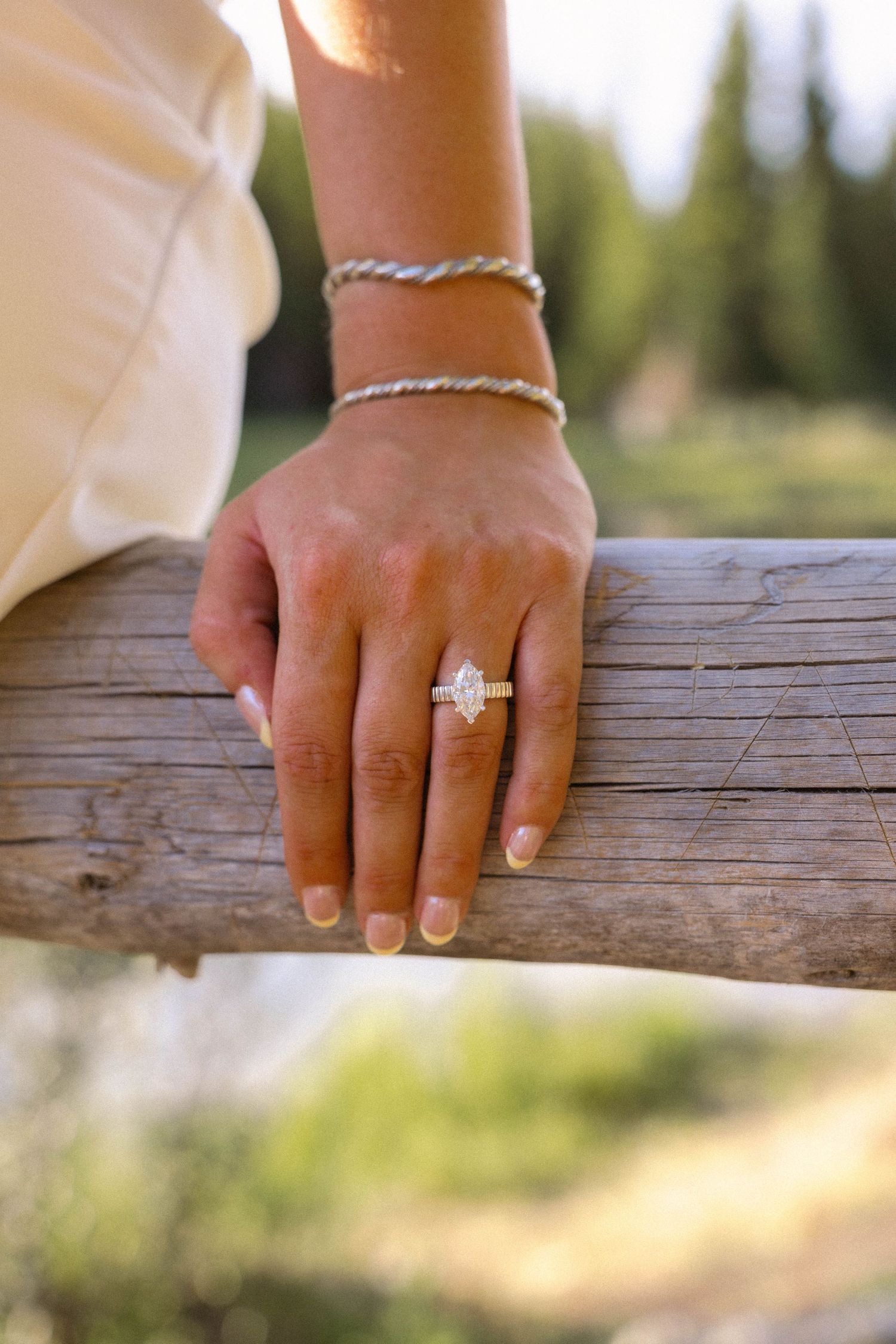Close-up of a marquise diamond engagement ring with halo setting on a woman's hand resting on a wooden fence.