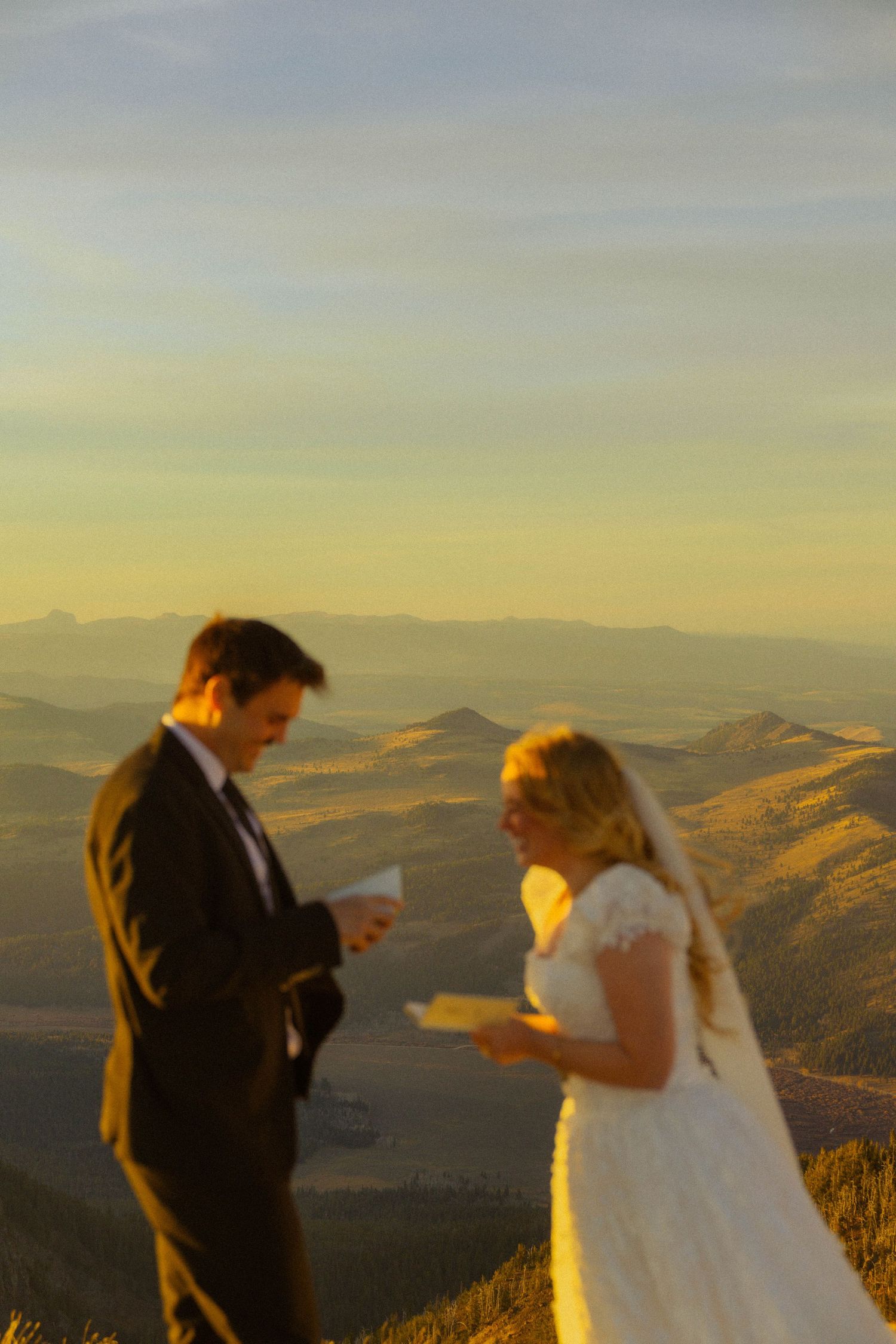 Bride and groom exchange vows on a mountain summit at golden hour with sweeping valley views behind them.