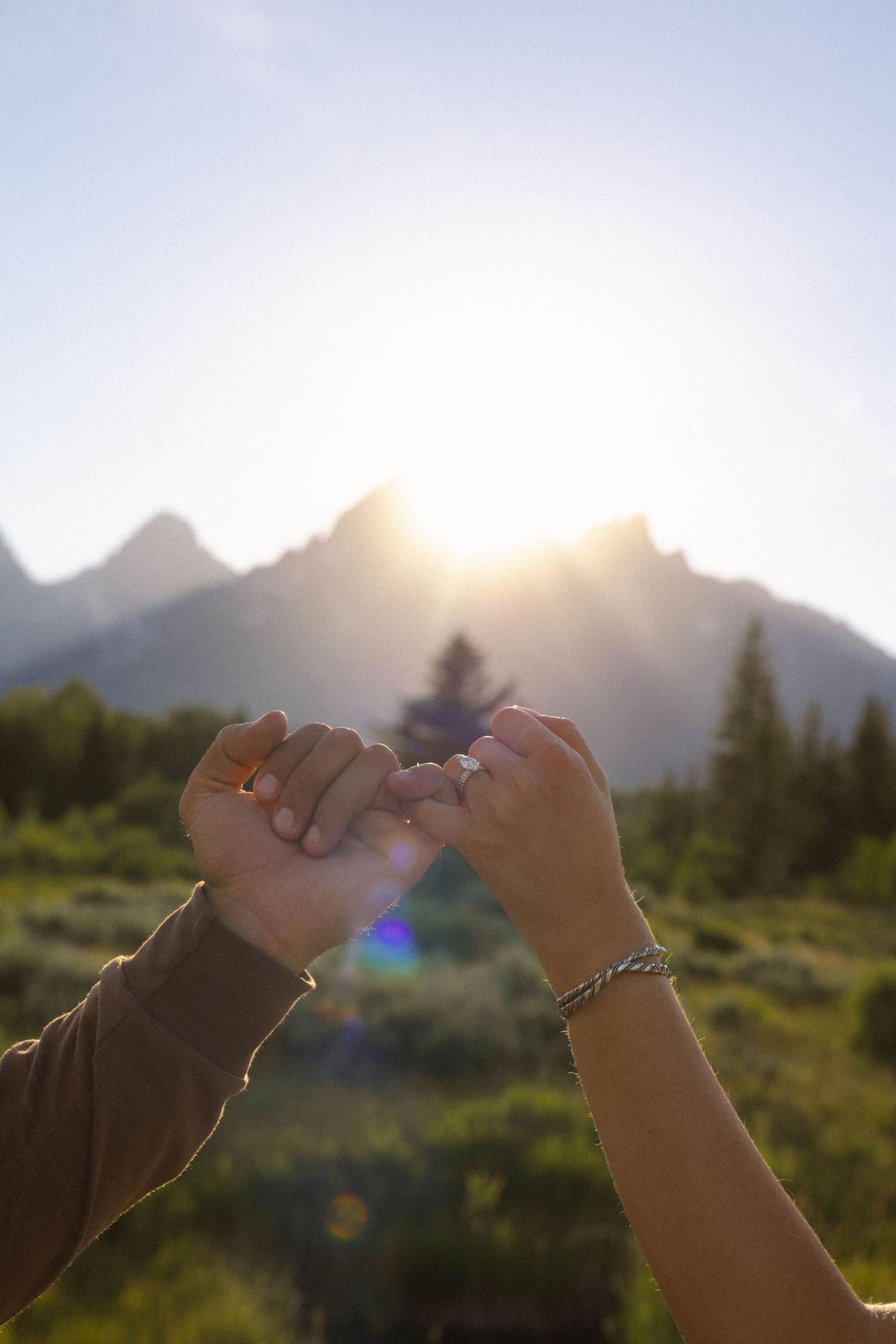 Two hands making a pinky promise at sunset with Grand Teton mountains in the background.