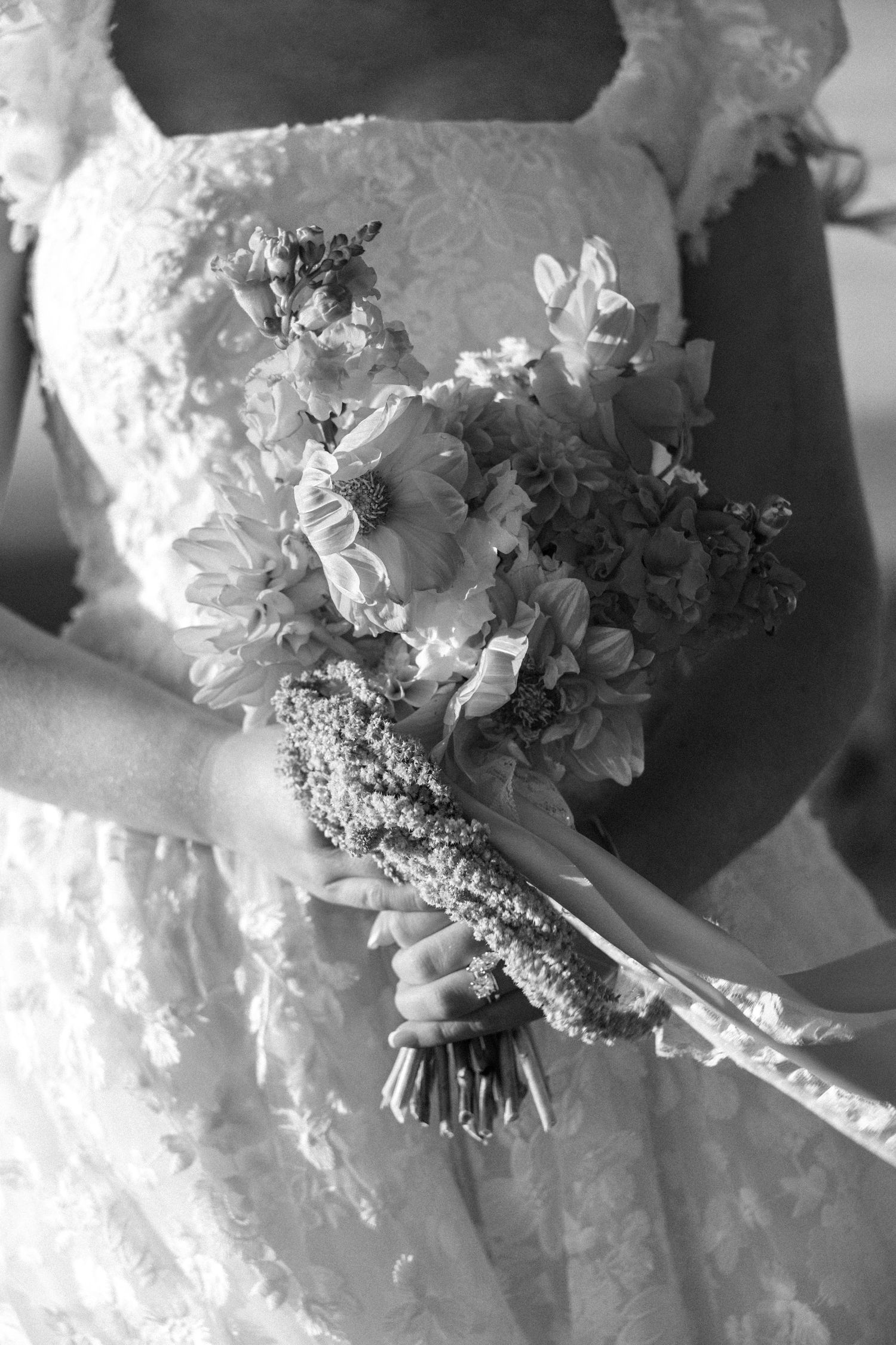 Bride holding a lush wedding bouquet of sunflowers and wildflowers in black and white photography.