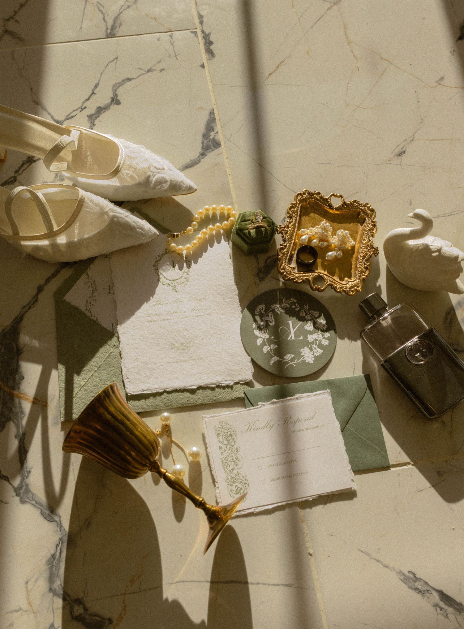 Elegant wedding flat lay with ivory heels, pearl bracelet, ornate jewelry box, invitations, and accessories on marble surface.