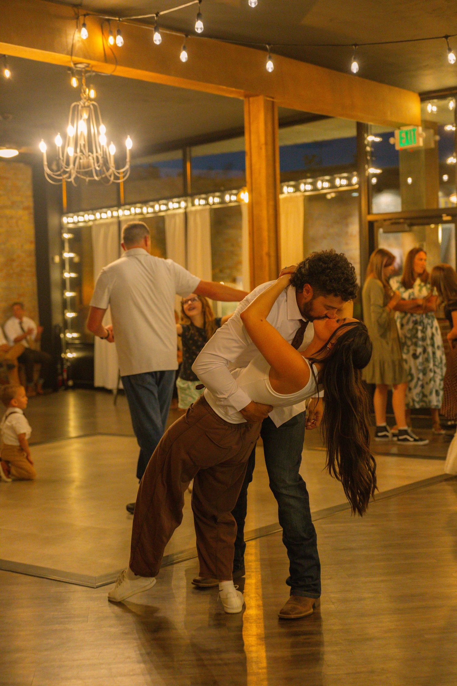 Couple sharing a romantic dip kiss on a warmly lit dance floor at an elegant indoor wedding reception.