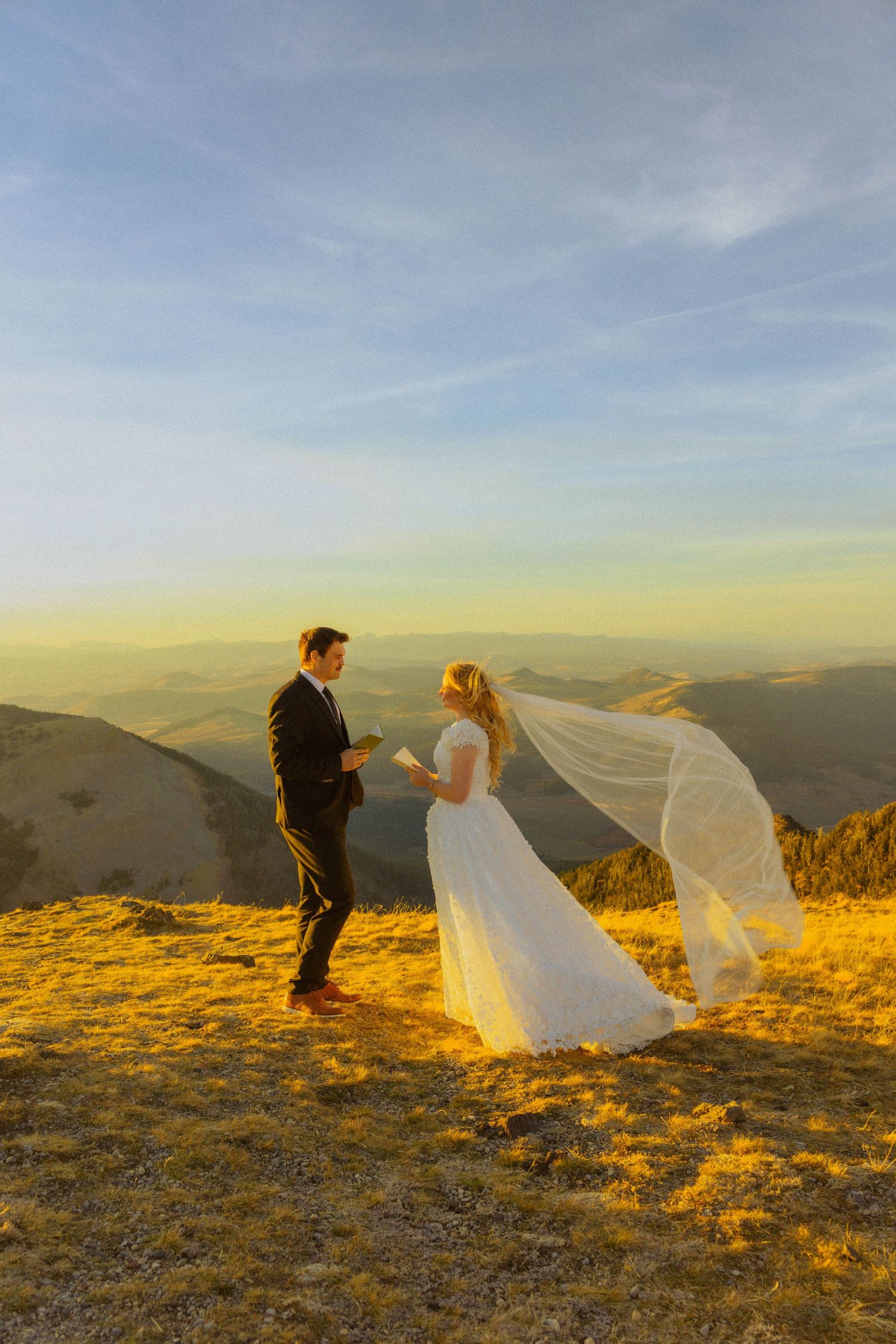 Bride and groom exchange vows on a mountain summit at golden hour, with veil flowing in the wind.
