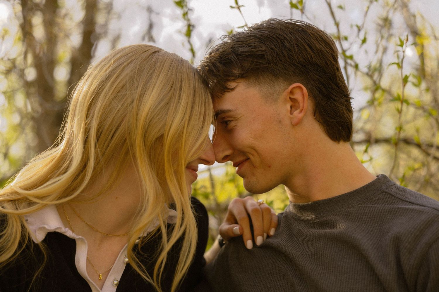 A young couple sharing a romantic moment outdoors, touching foreheads and smiling among spring blossoms.