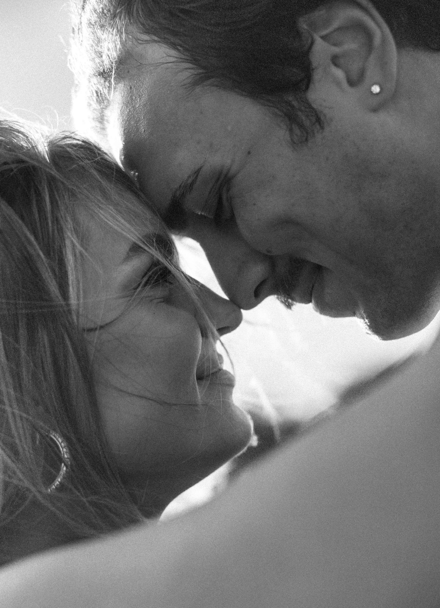 Black and white romantic photo of a smiling couple leaning in close, foreheads nearly touching in an intimate moment.