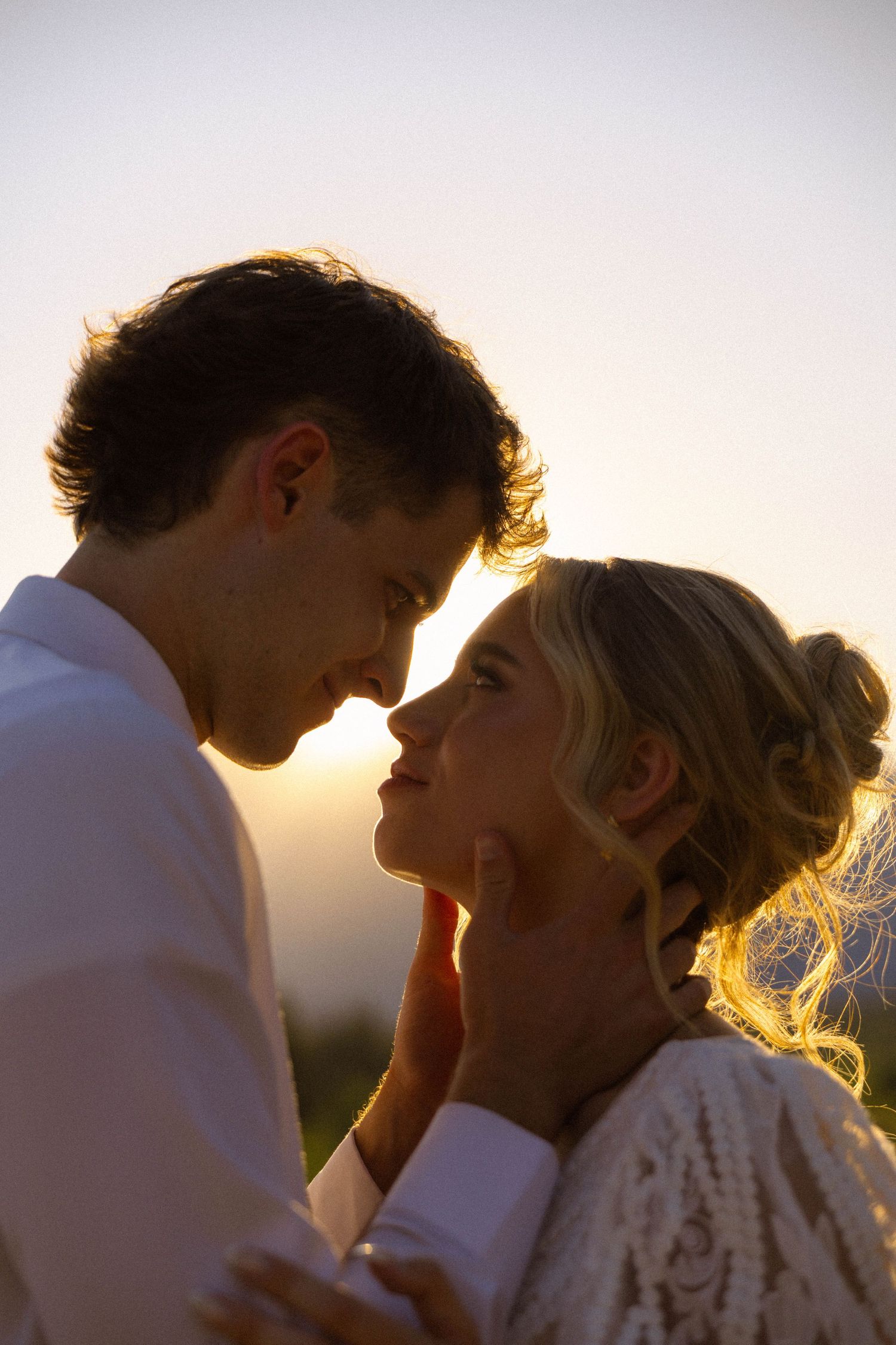 Romantic couple sharing an intimate moment at golden hour sunset, almost kissing in warm backlit glow.