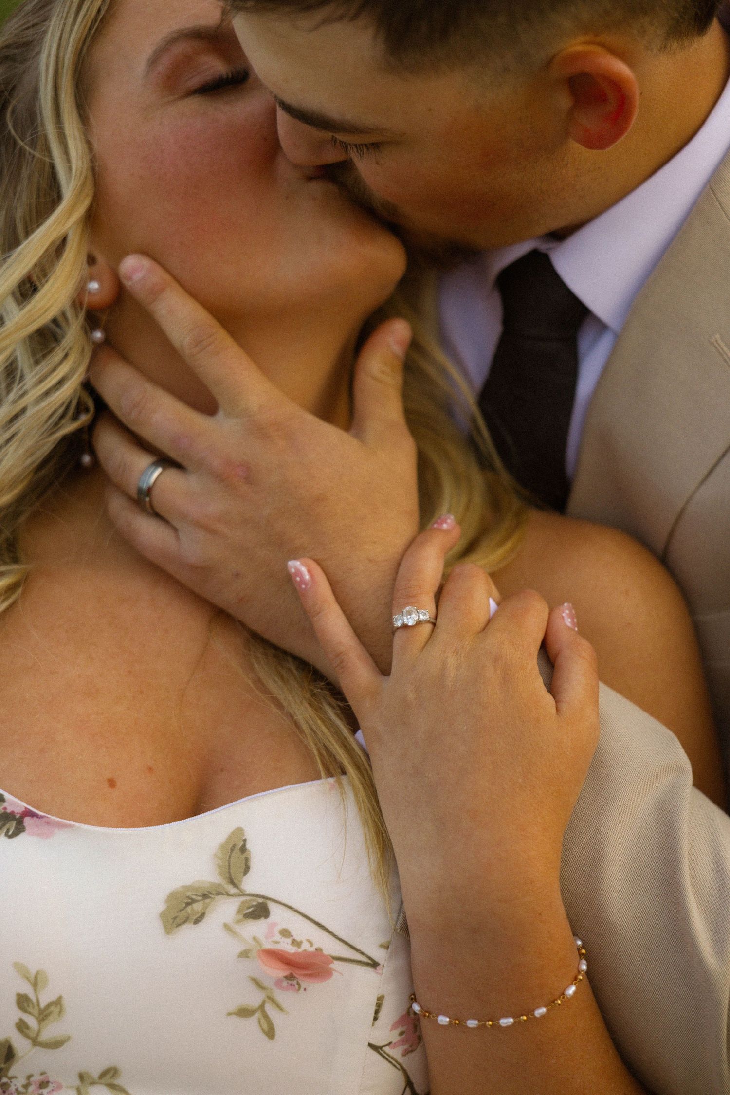 Couple sharing a romantic kiss, showcasing an engagement ring and bracelet on the bride's hand in a close-up wedding photo.