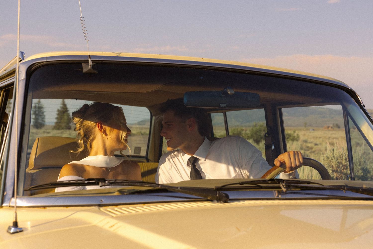 Couple riding in a vintage yellow van through scenic countryside on a sunny day.