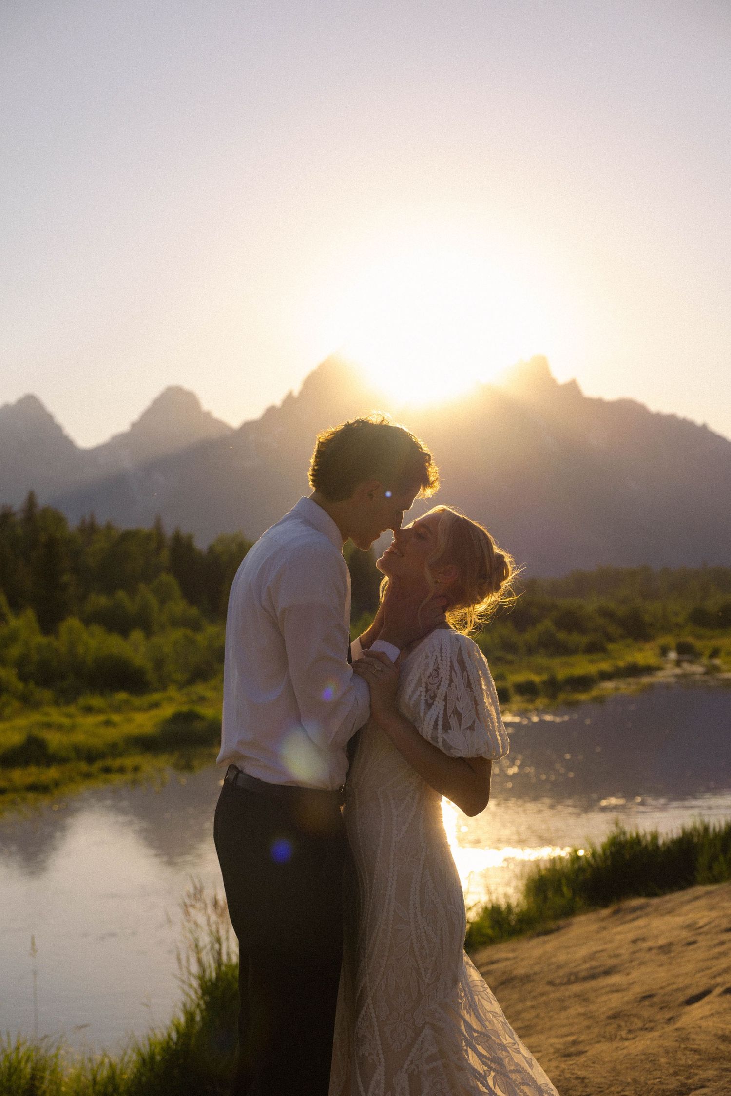 Bride and groom share romantic moment at sunset with Grand Teton mountains and river in background.