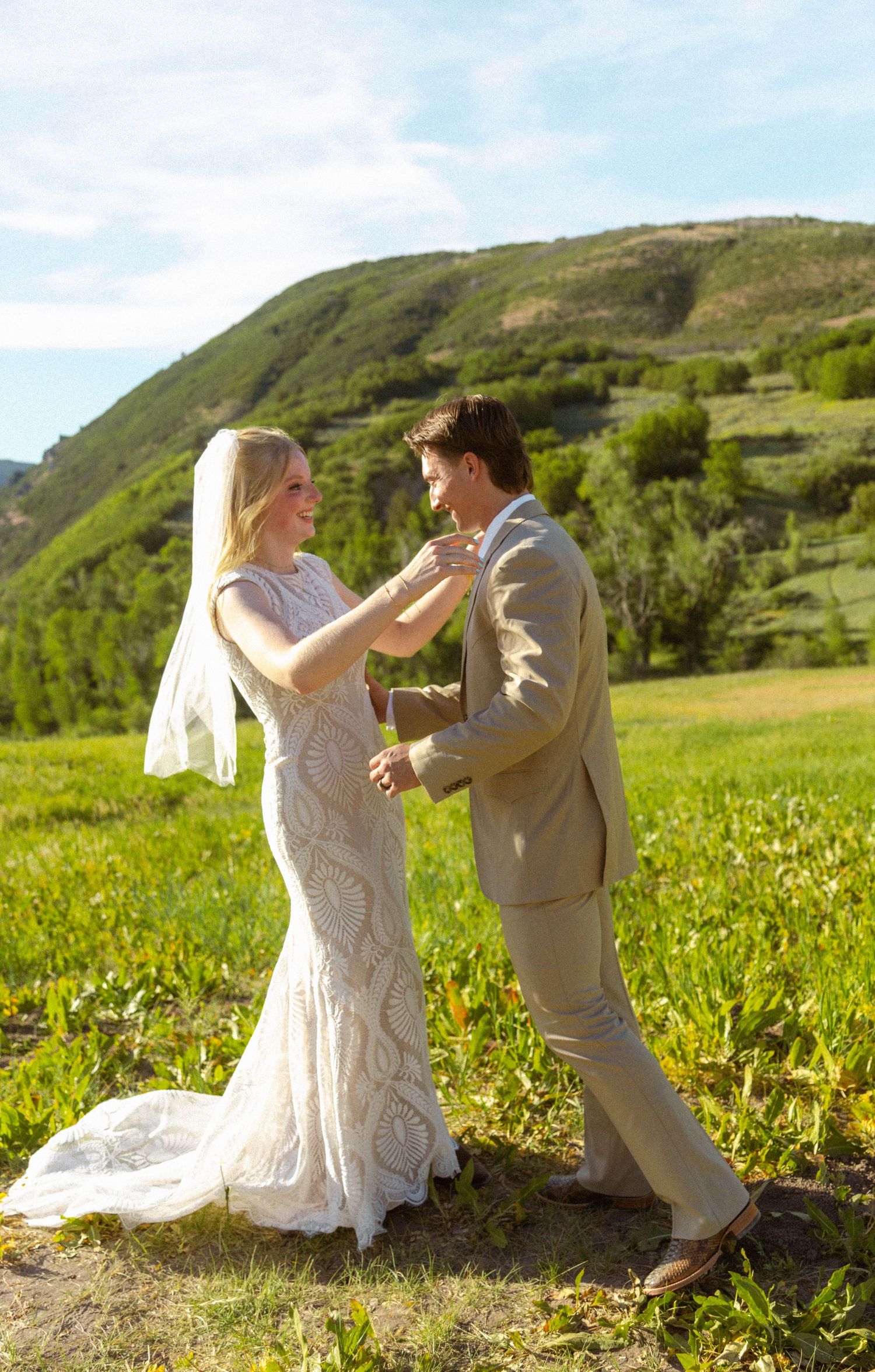 Bride and groom dancing in a sunny green meadow with rolling hills, bride in lace gown with veil.