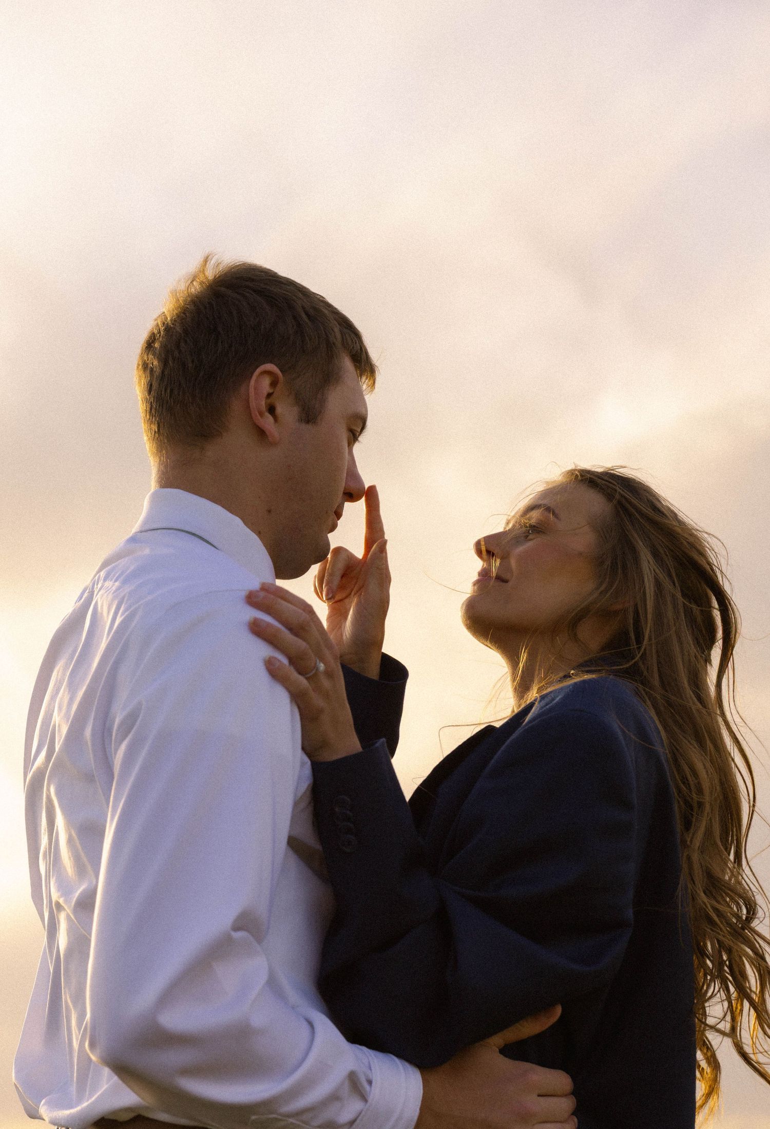 Romantic couple embracing at sunset, woman touching man's face tenderly against a golden sky backdrop.
