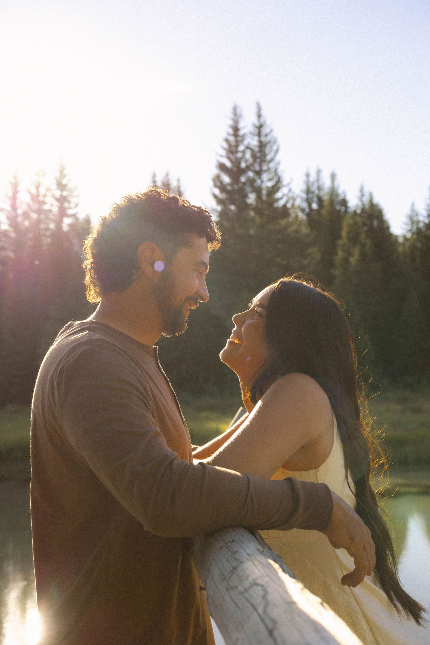 Romantic couple sharing a tender moment outdoors near a forest lake in warm golden sunlight.