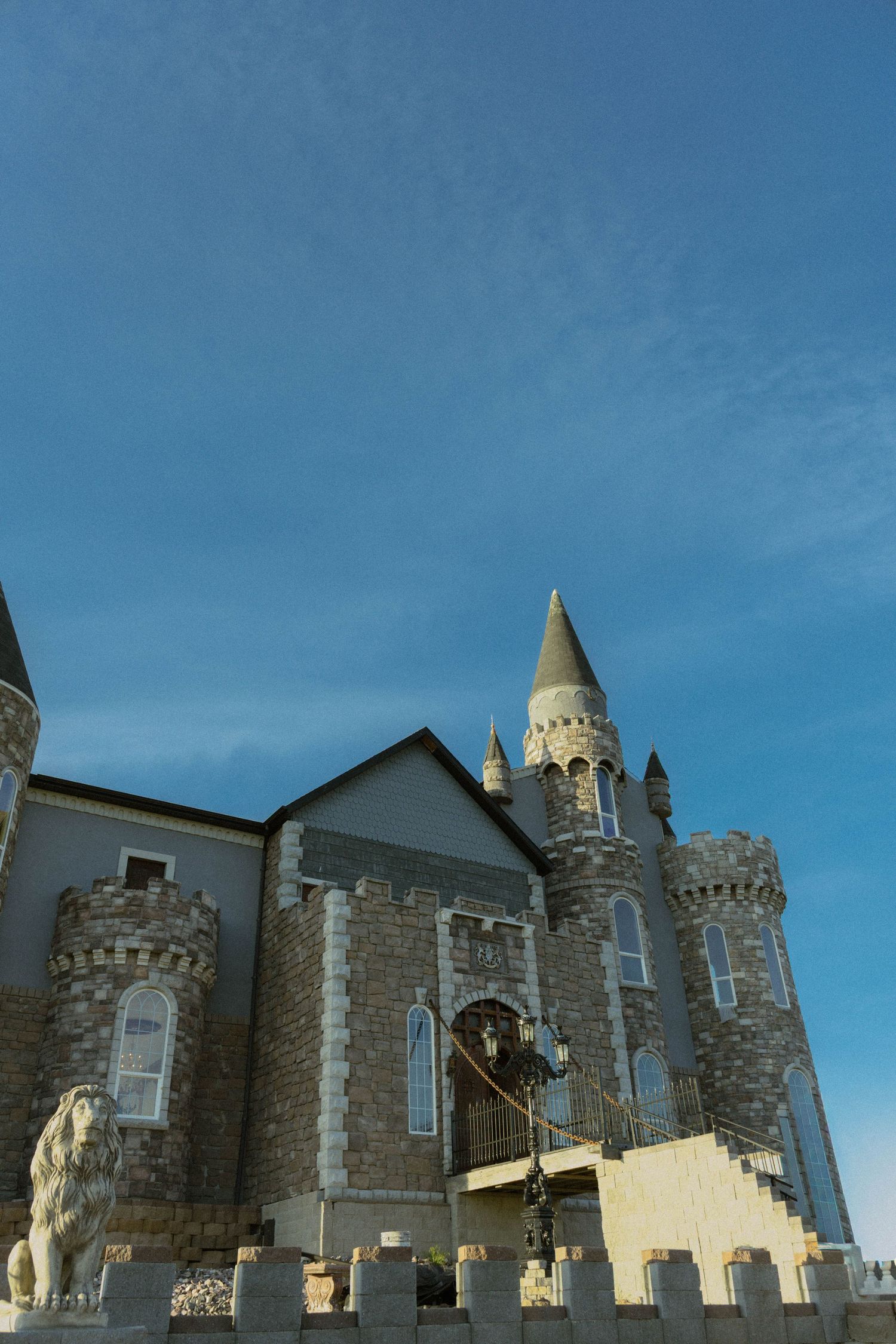 Stone castle with pointed tower and lion statues under blue sky.