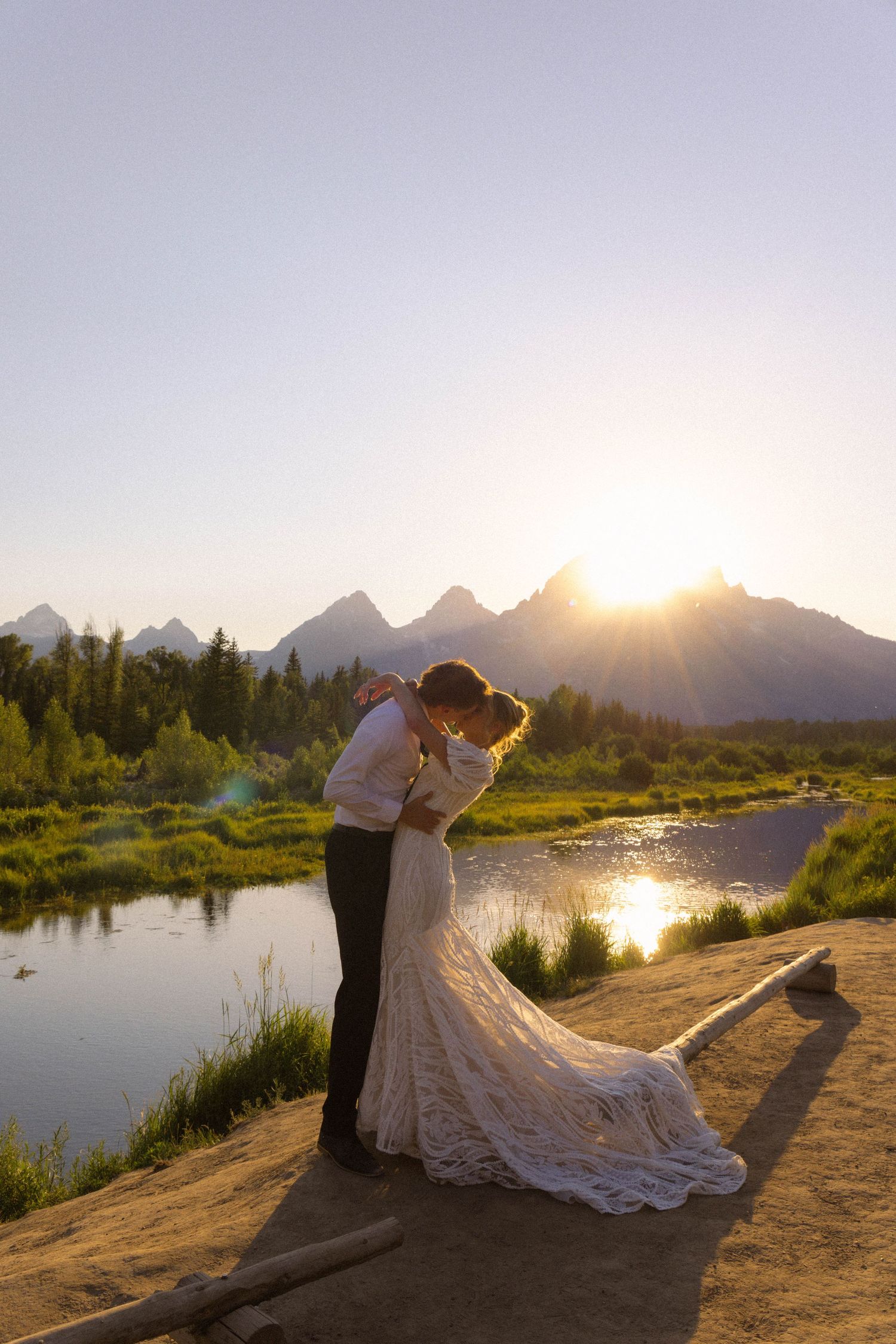 Bride and groom share a sunset kiss at Grand Teton National Park with mountains and river backdrop.