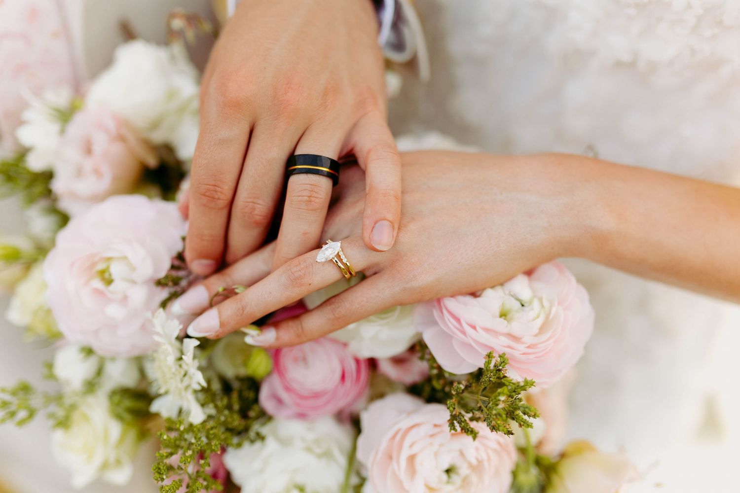 Newlywed couple displaying wedding rings over a bouquet of pink and white roses.