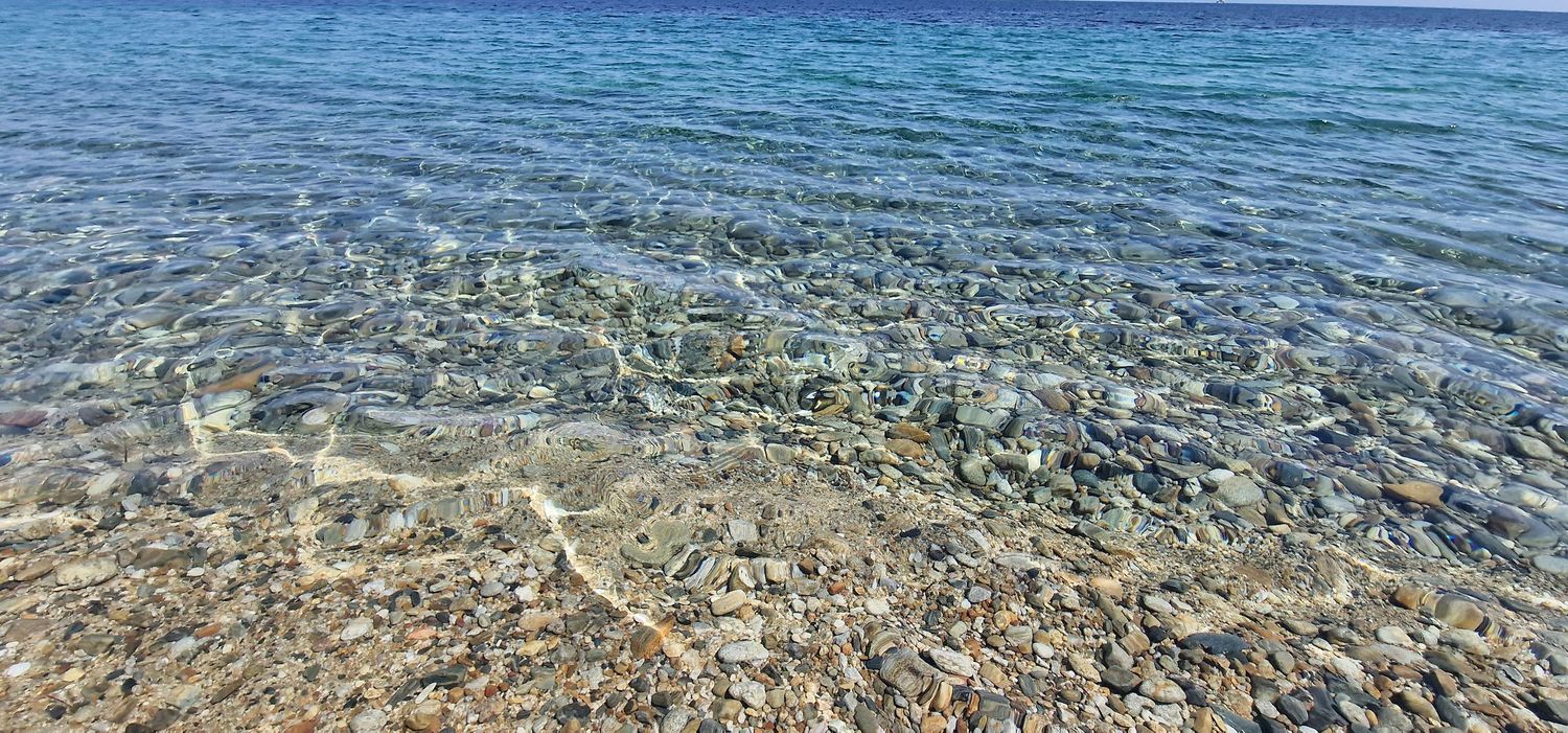 Crystal clear shallow ocean water lapping over a pebble beach with turquoise blue sea in the background.
