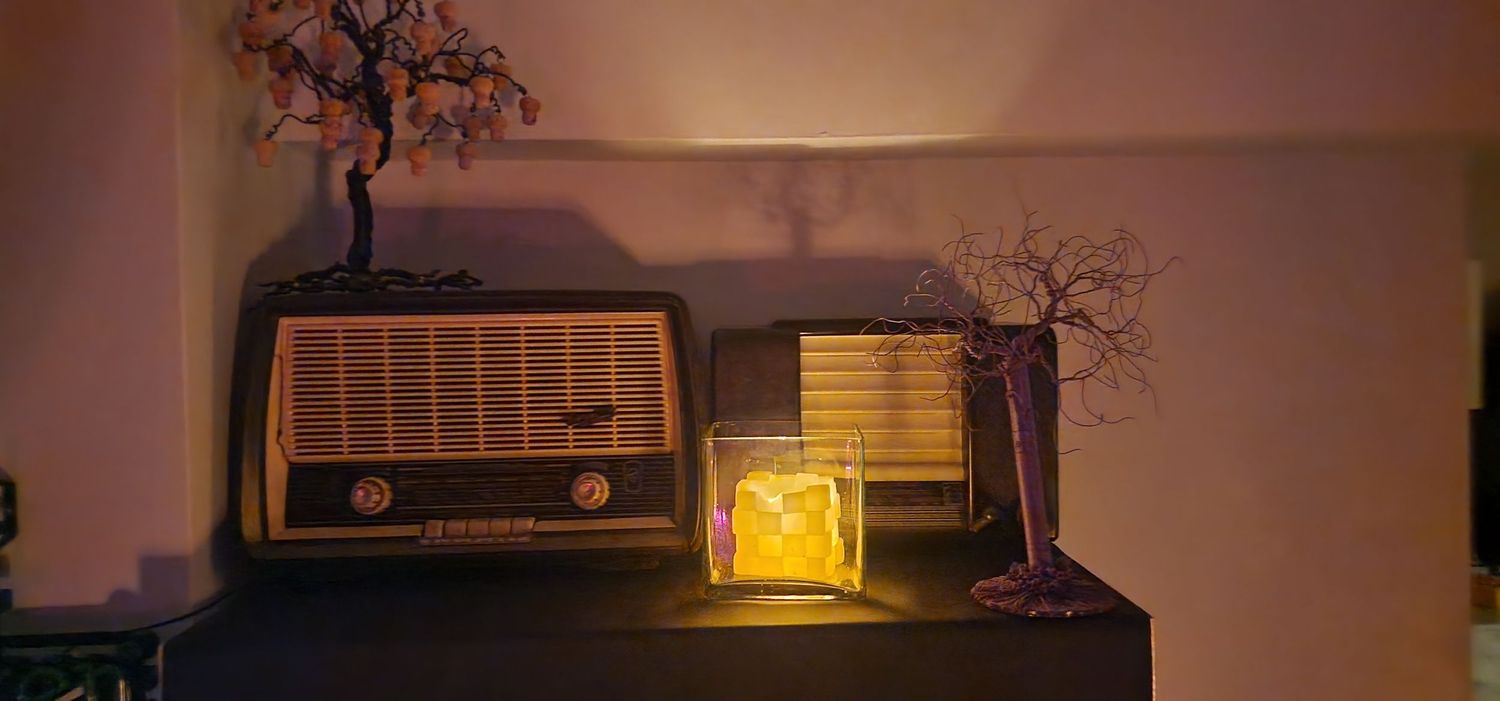 Retro wooden radio beside illuminated lamp and bonsai trees on dark shelf.