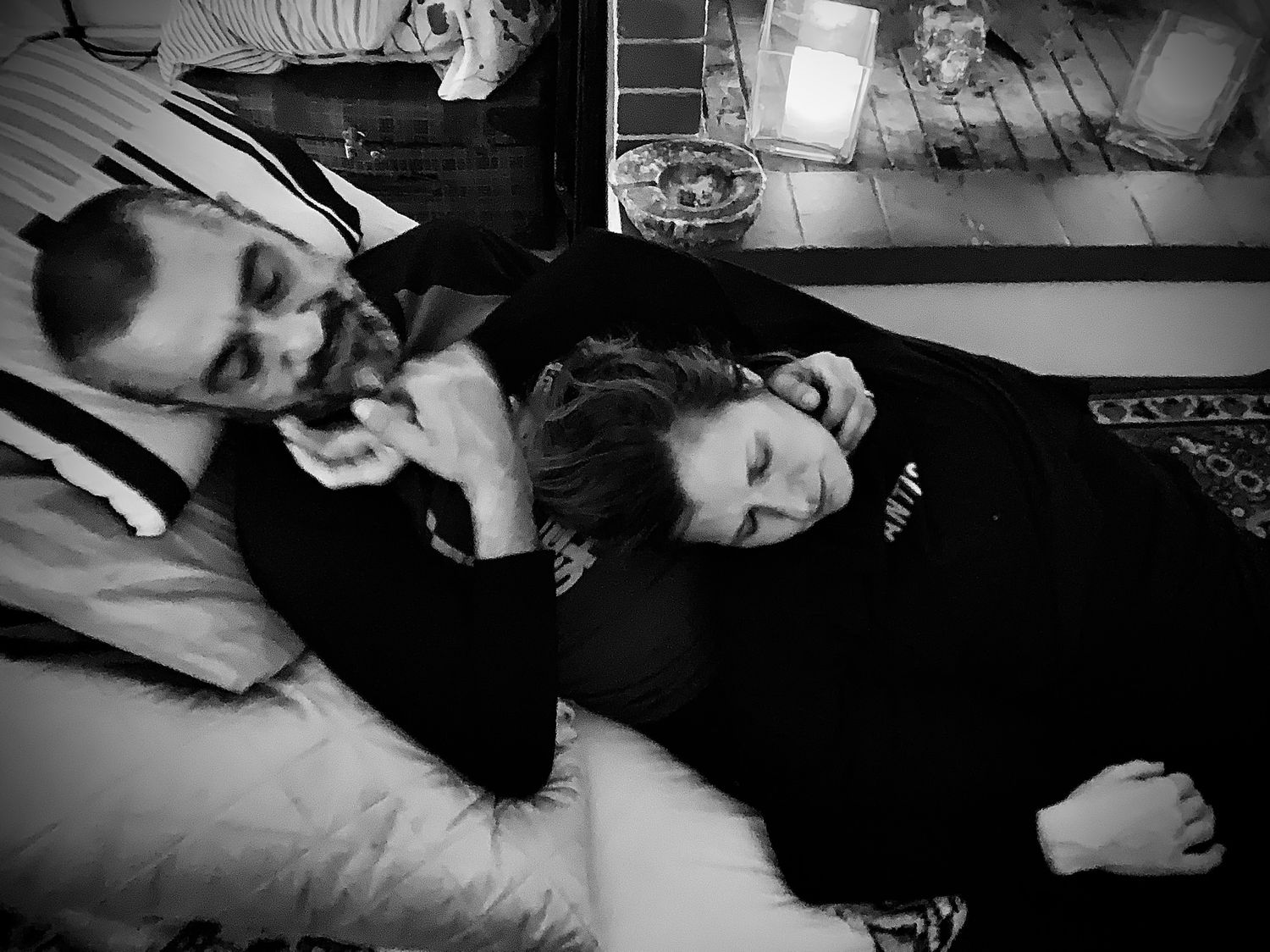 Black and white photo of two people resting together on a bed indoors.