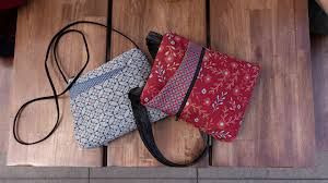 Two fabric crossbody bags on wood, one grey geometric print and one red floral pattern.