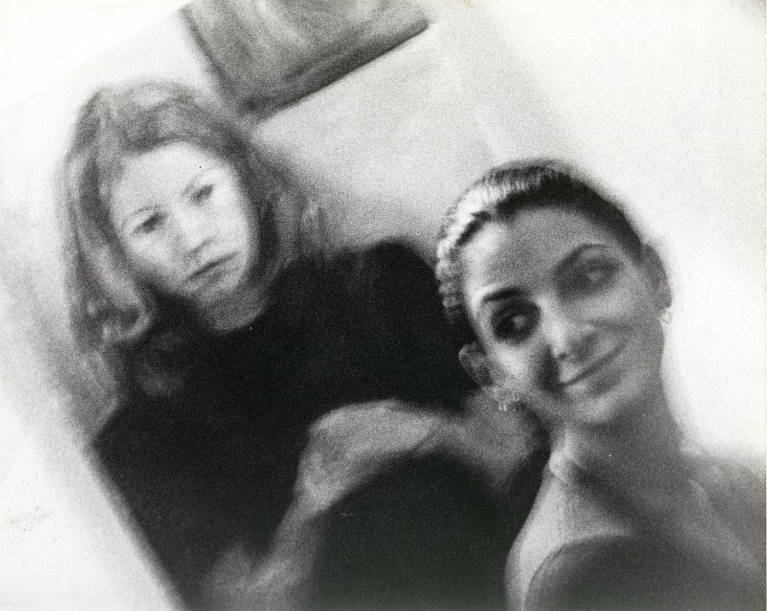 Black and white photo of two women smiling together in a softly lit, vintage-style portrait.