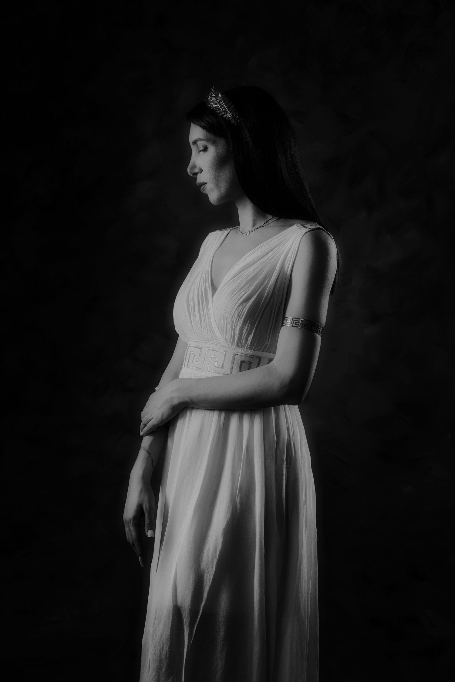 Black and white studio portrait of a woman in a white flowing dress with a decorative headband.
