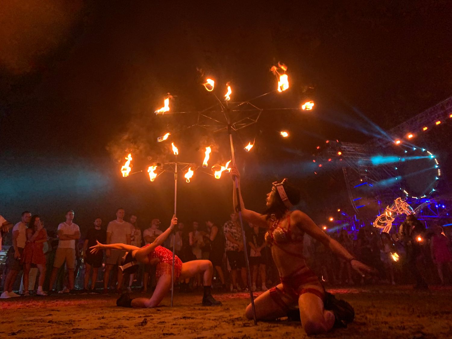 Fire dancers performing with spinning flaming props before crowd at vibrant outdoor beach night festival.